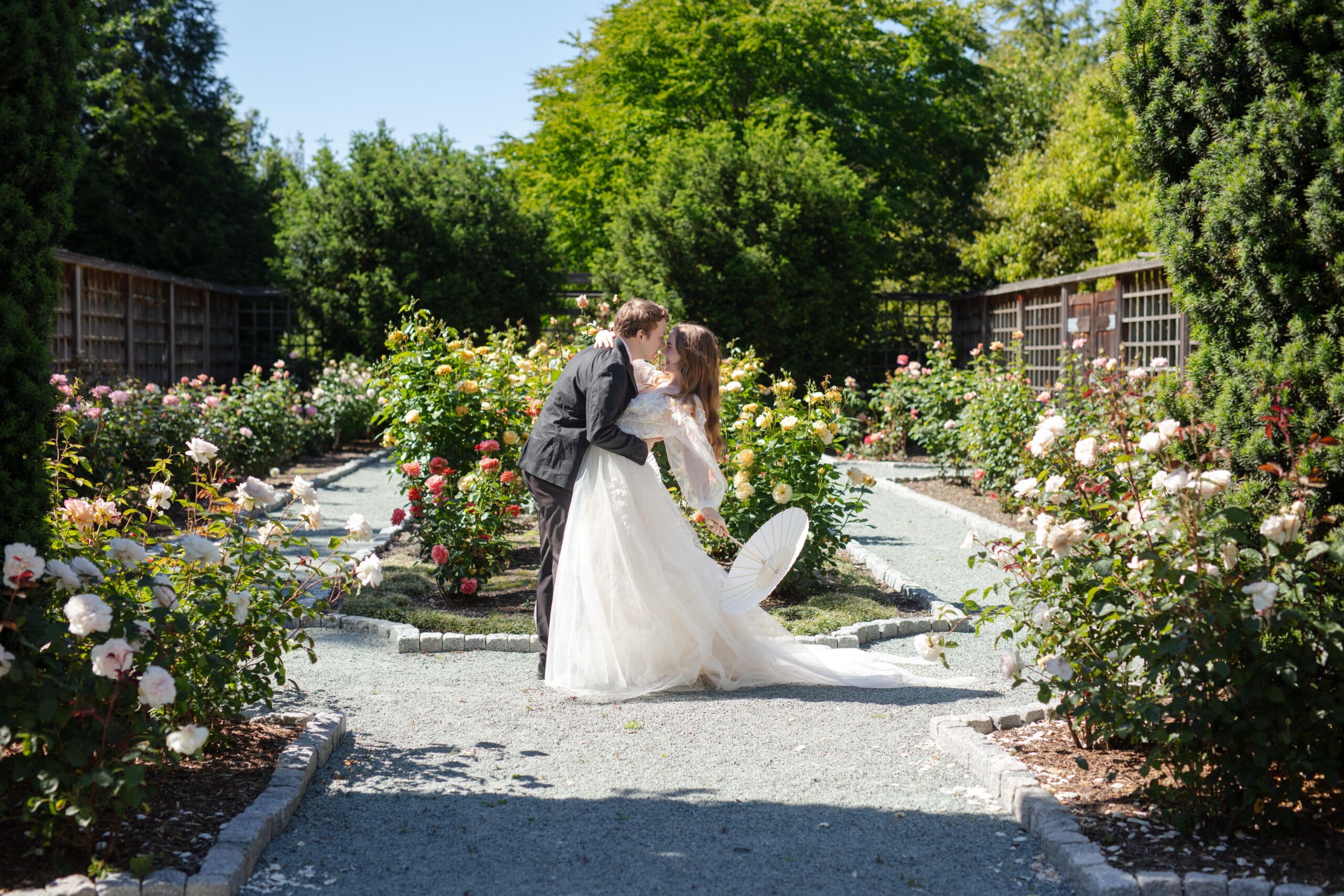 Bride and groom sharing a kiss in a blooming garden pathway, captured by a Washington wedding photographer focused on romantic, story-led moments.