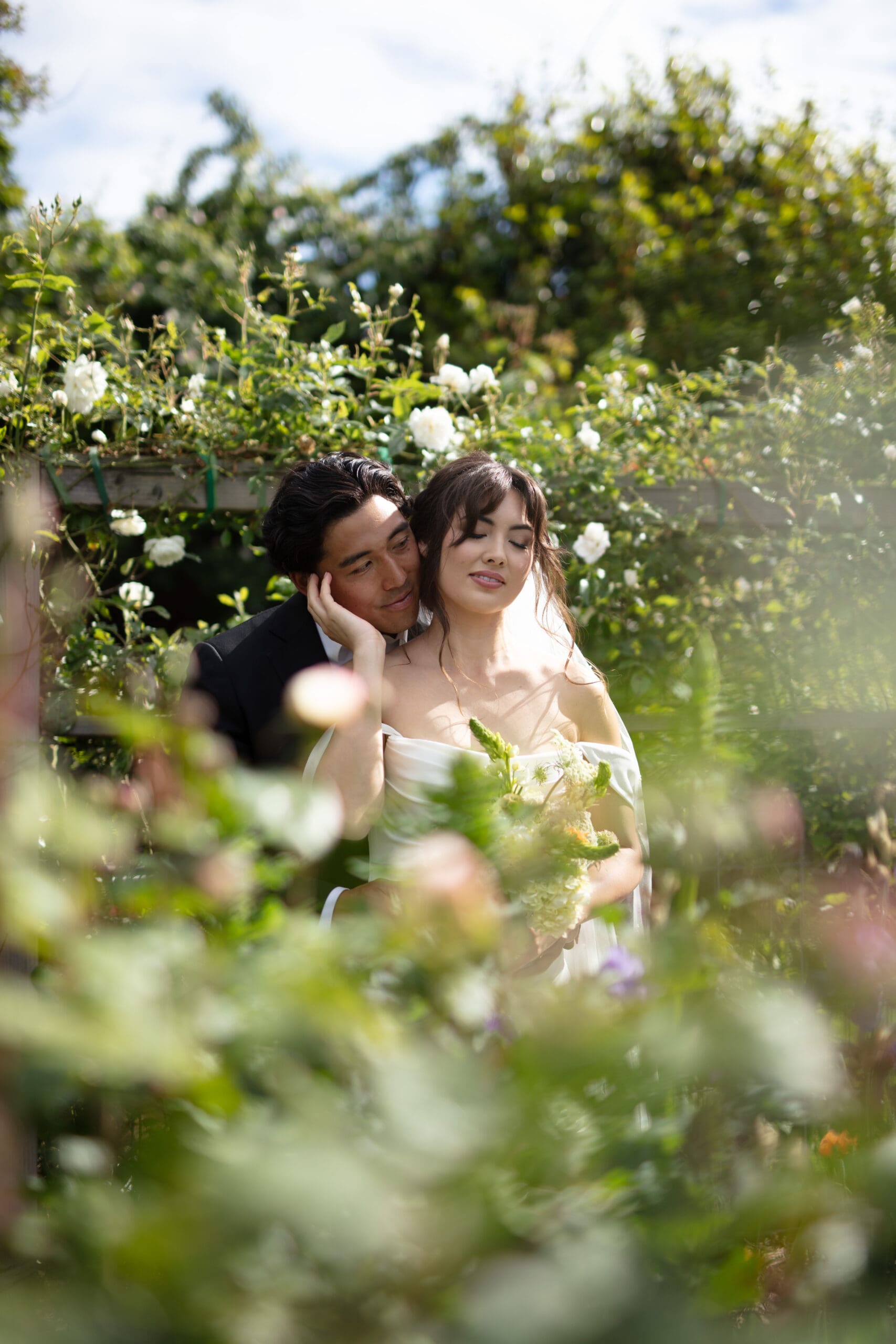 Tender portrait of a couple wrapped in each other’s arms among blooming white roses, captured by a Washington wedding photographer.