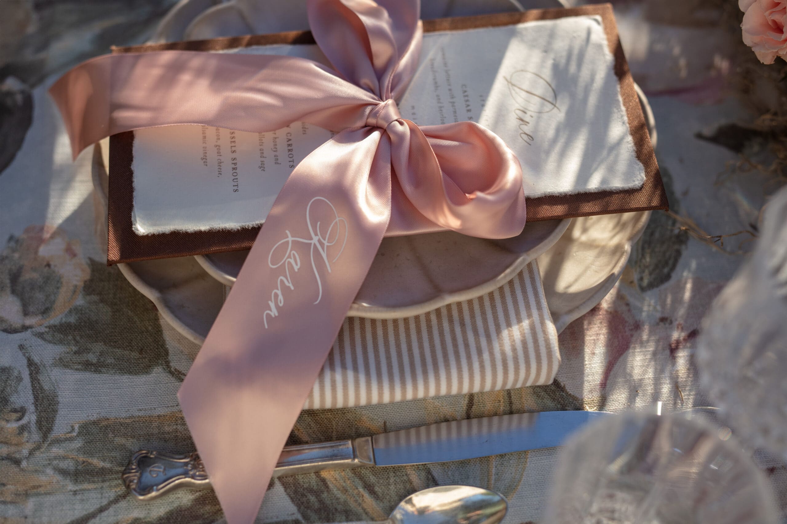Soft pink silk ribbon tied over a wedding menu in a romantic flat lay of thoughtful, personalized reception details.
