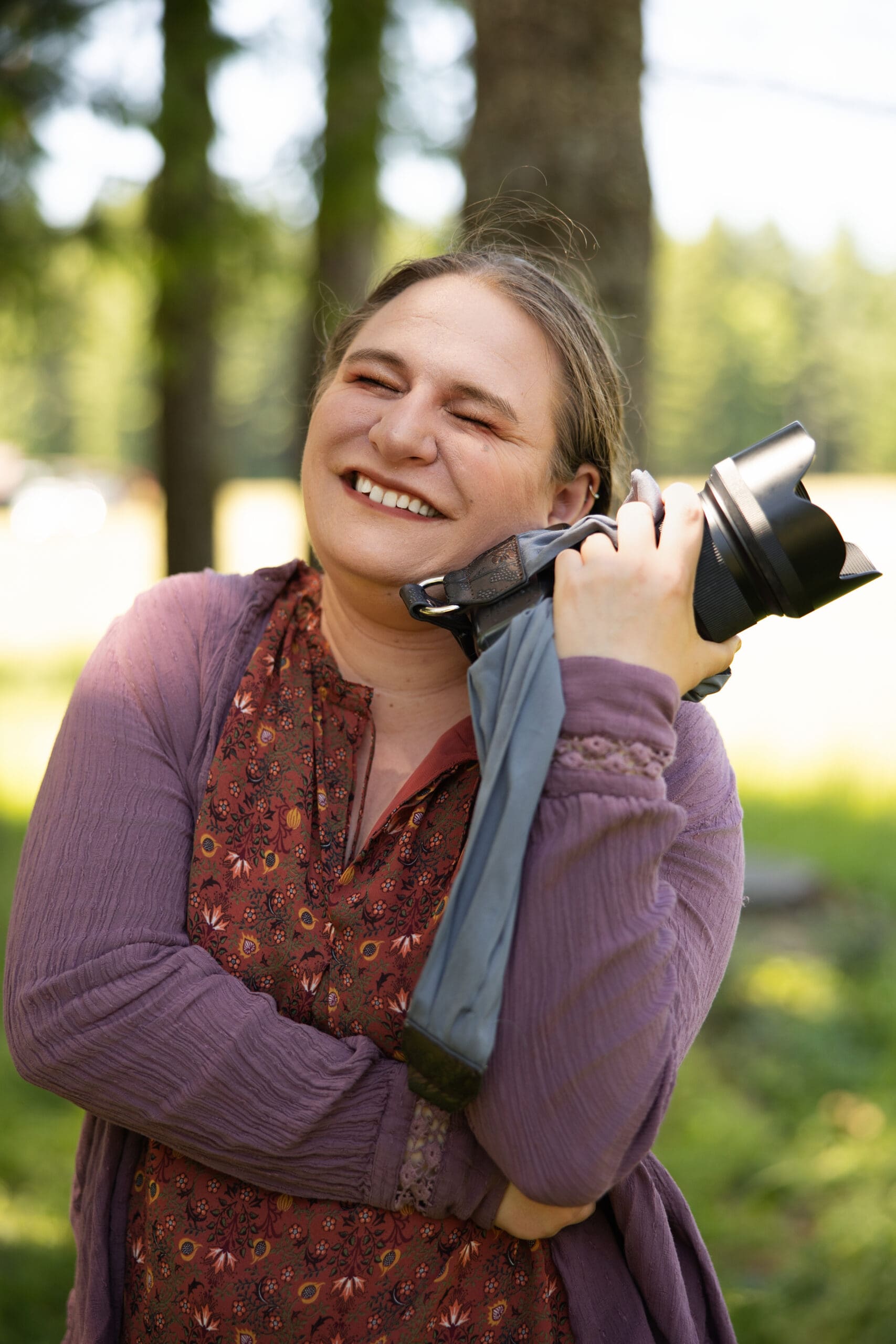 Washington wedding photographer captured laughing with her camera, blending warmth and joy with a nature-inspired backdrop.