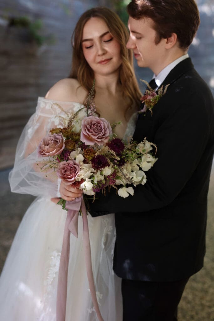 Bride holding her bouquet while groom admires her during their portrait session at Briarwood Estate.

