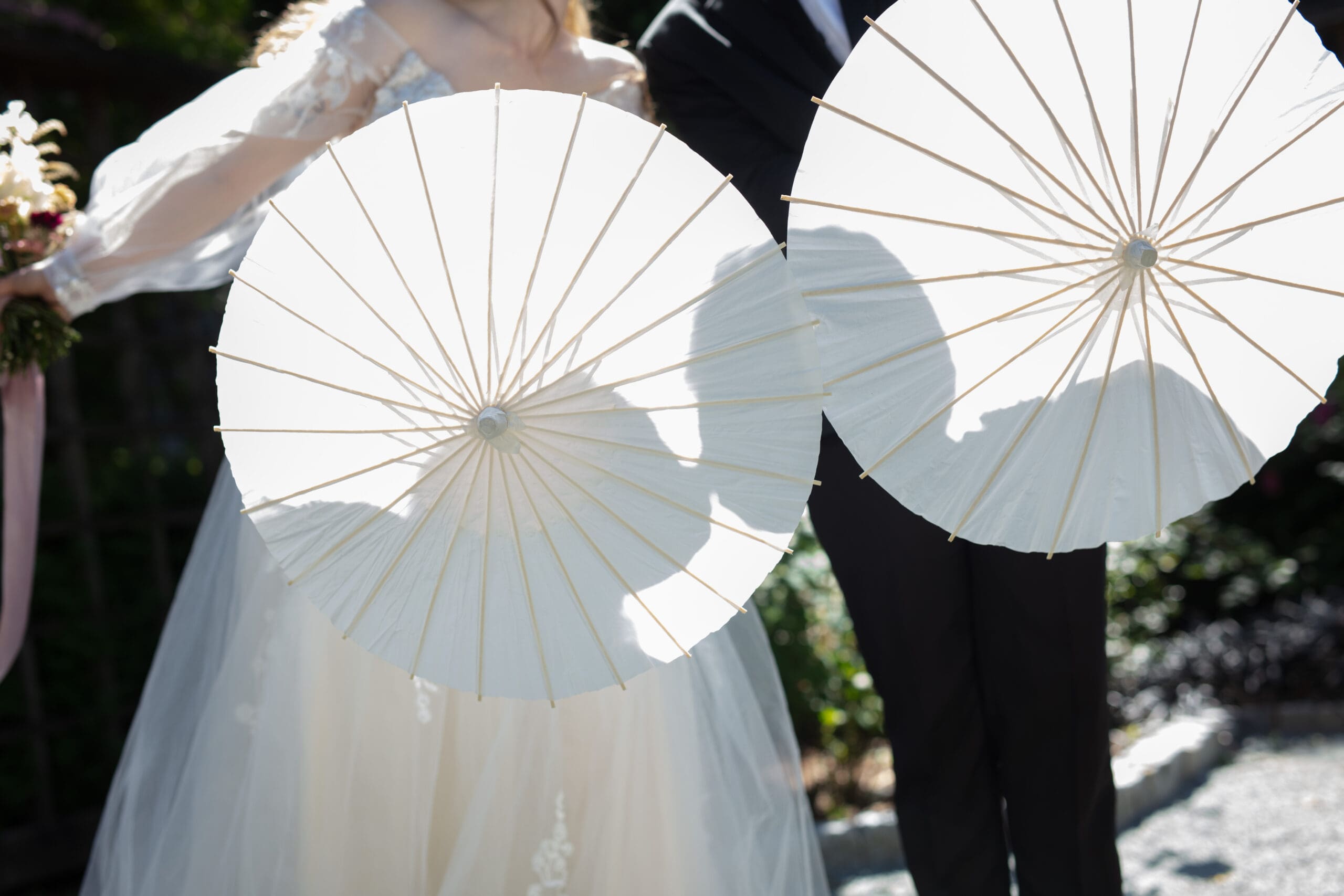 Couple holding white parasols while walking through the garden at chic and romantic wedding venue