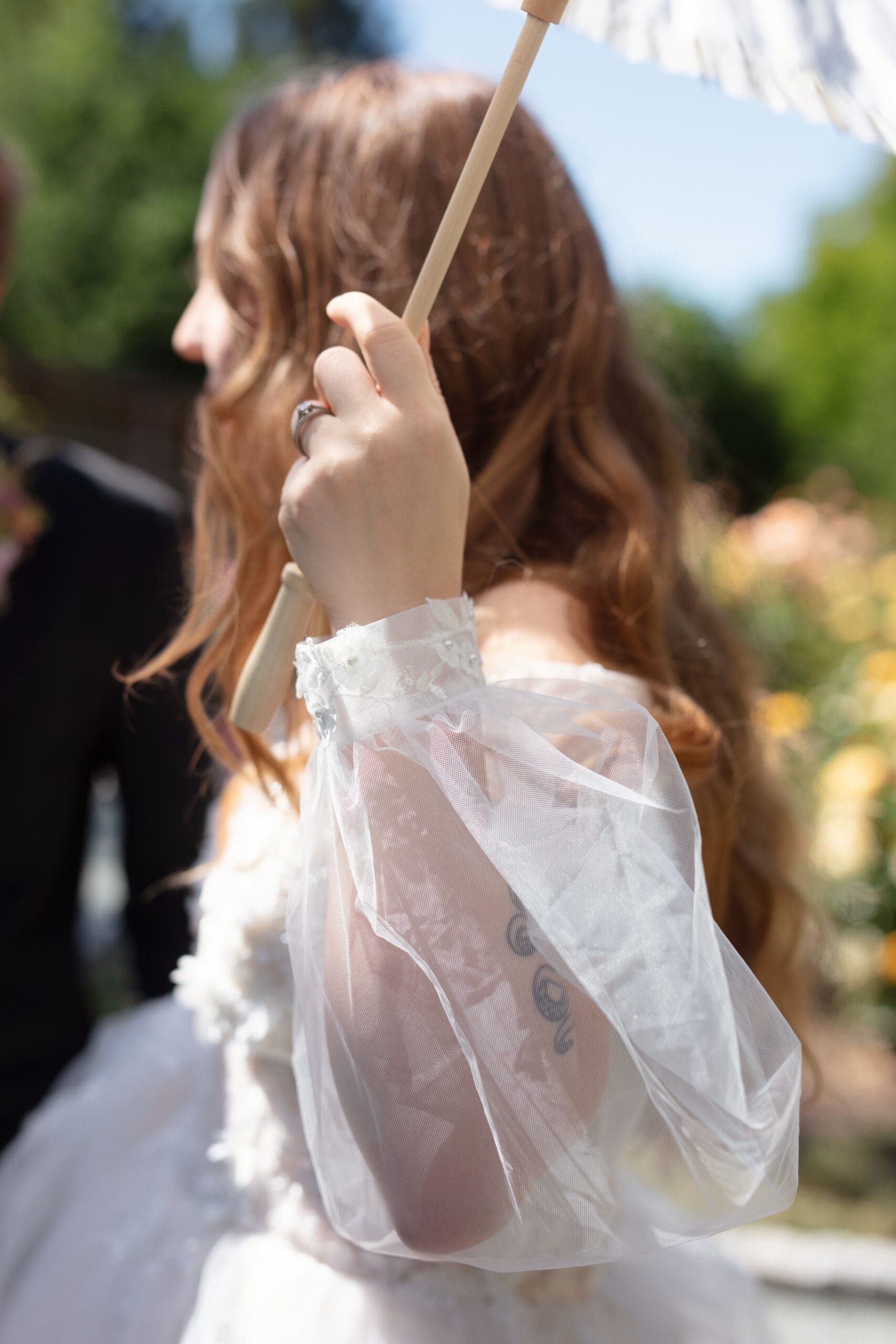 Detail shot of bridal sleeve and parasol during a sunny garden shoot.