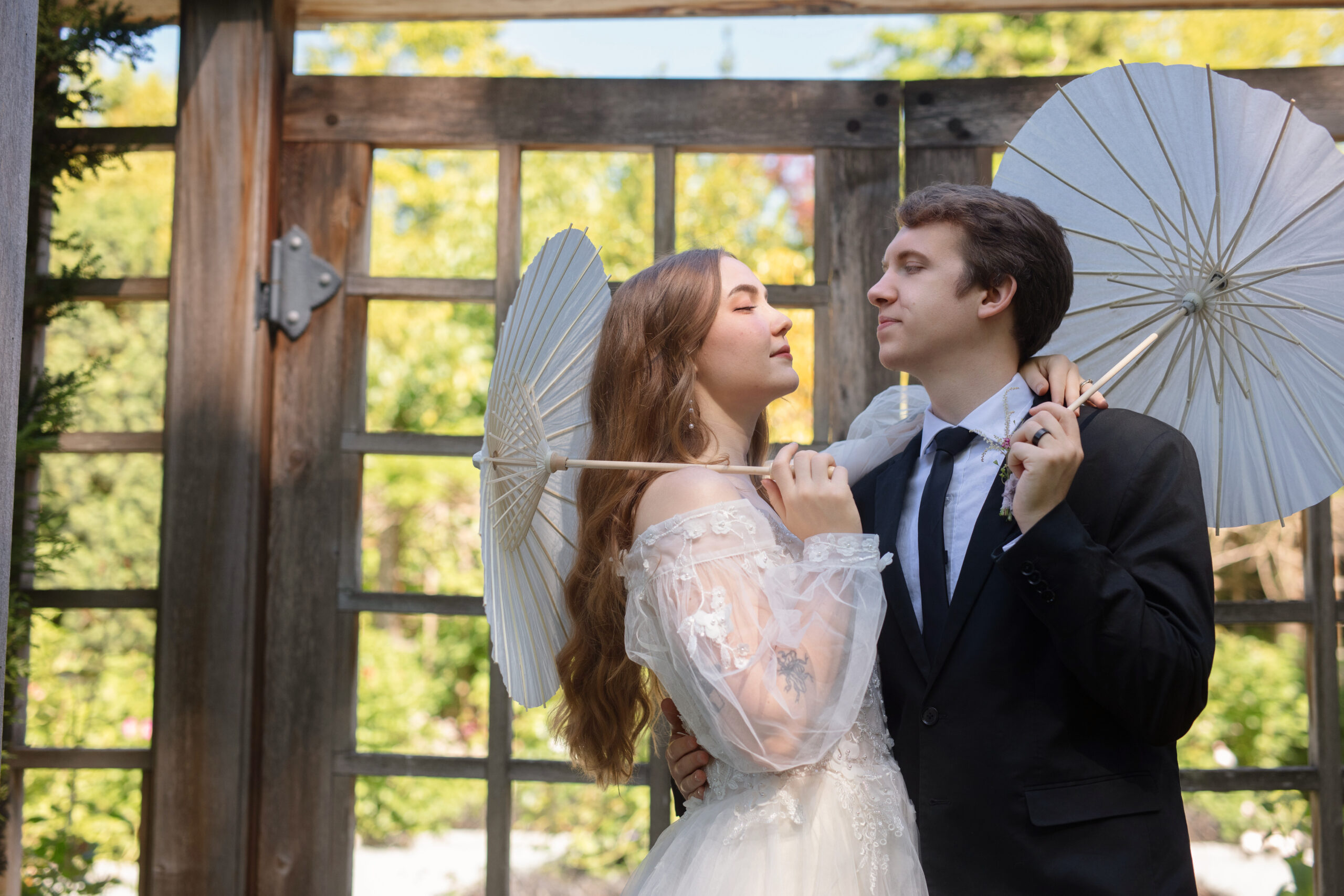 Elegant couple posing under rustic arch with parasols at Briarwood Estate.