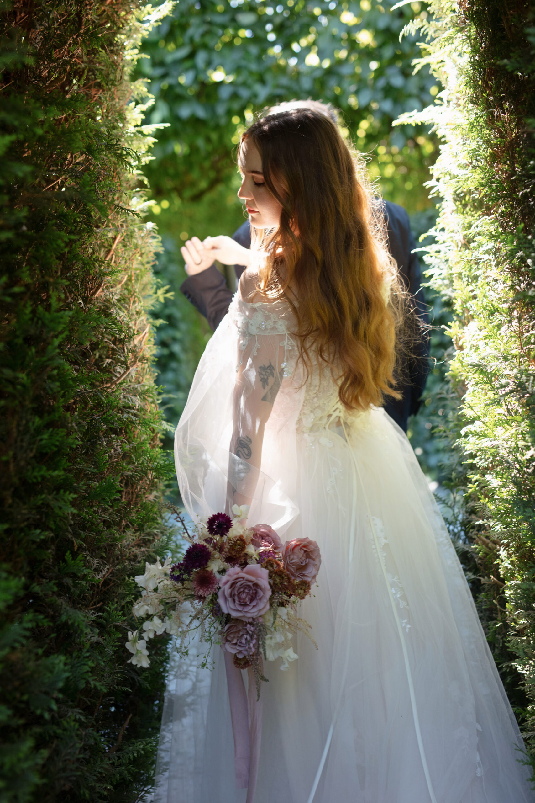 Bride in lace gown framed by hedges and soft light at Briarwood Estate.