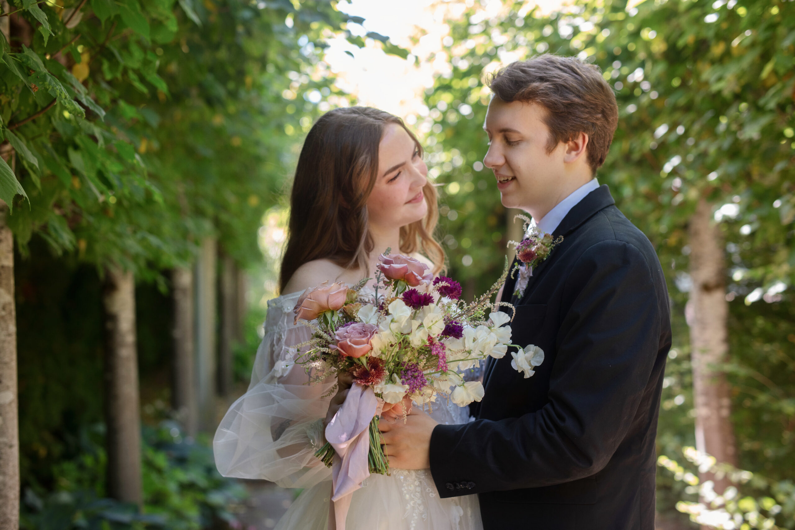 Bride and groom exchanging a loving glance surrounded by tall greenery.