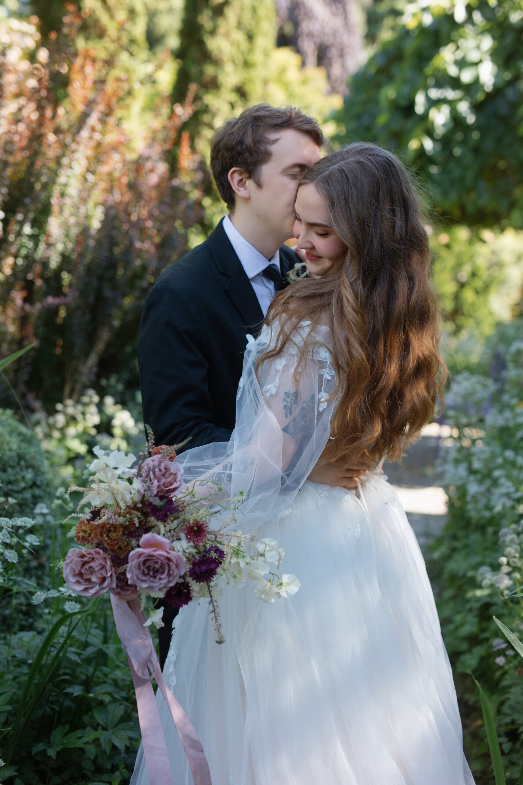 Groom embracing bride in lush green garden at Briarwood Estate.