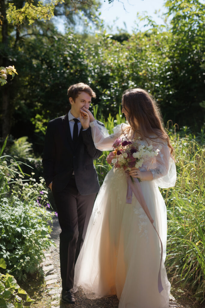 Groom kisses bride’s hand as they stroll through the gardens at Briarwood Estate.