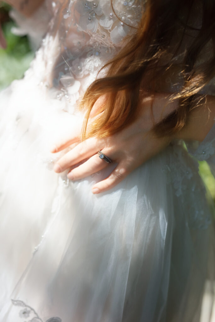 Close-up of bride’s engagement ring resting on her lace wedding gown.