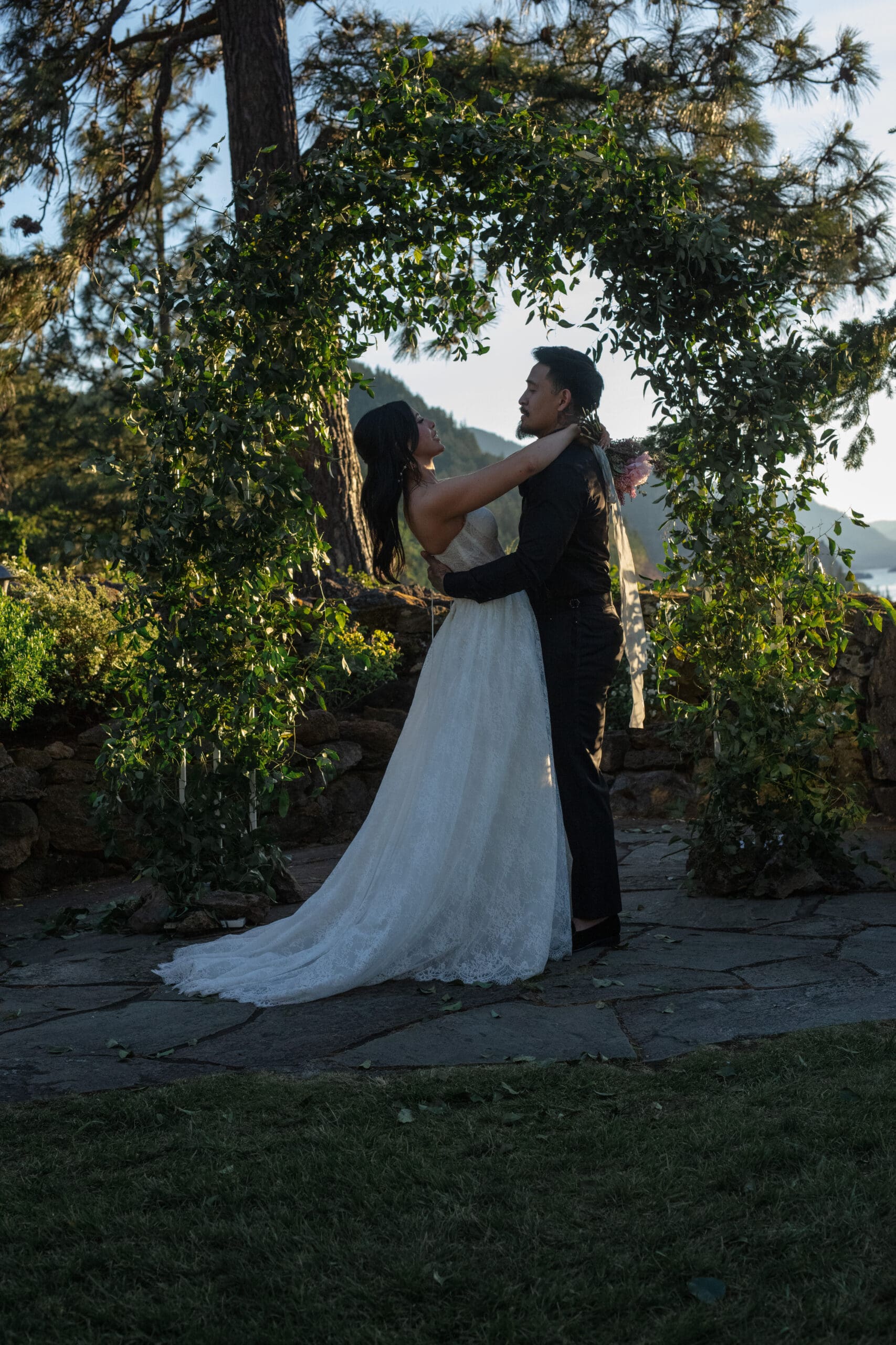 Couple sharing an embrace beneath a greenery-covered arch during their Griffin House wedding ceremony