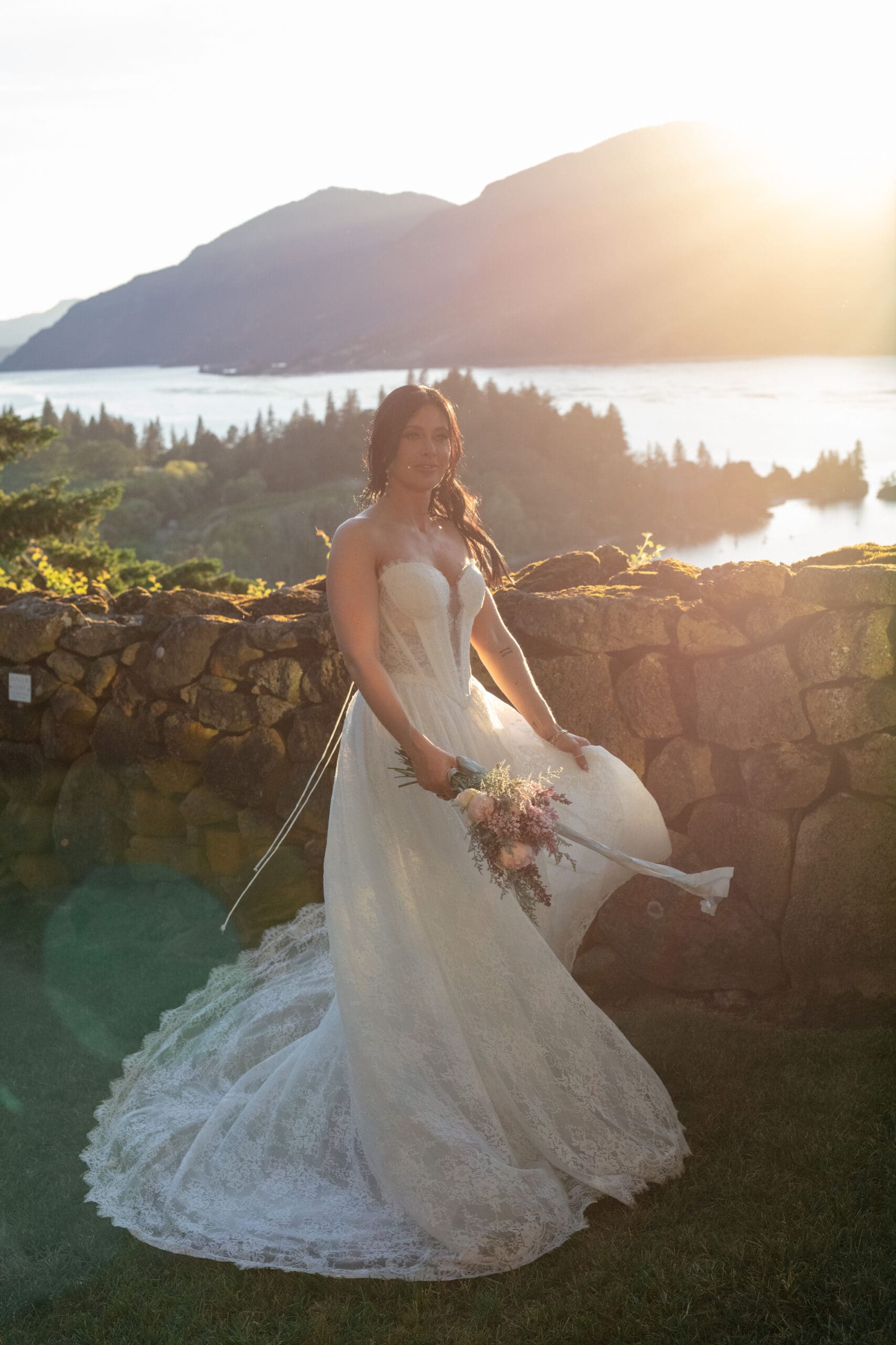Bride holding bouquet in front of stone wall at golden hour, overlooking the Columbia River Gorge