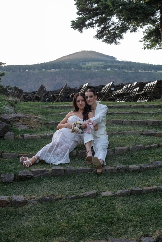 Two brides sitting close on stone steps at The Griffin House with mountain views in the background — The Griffin House wedding