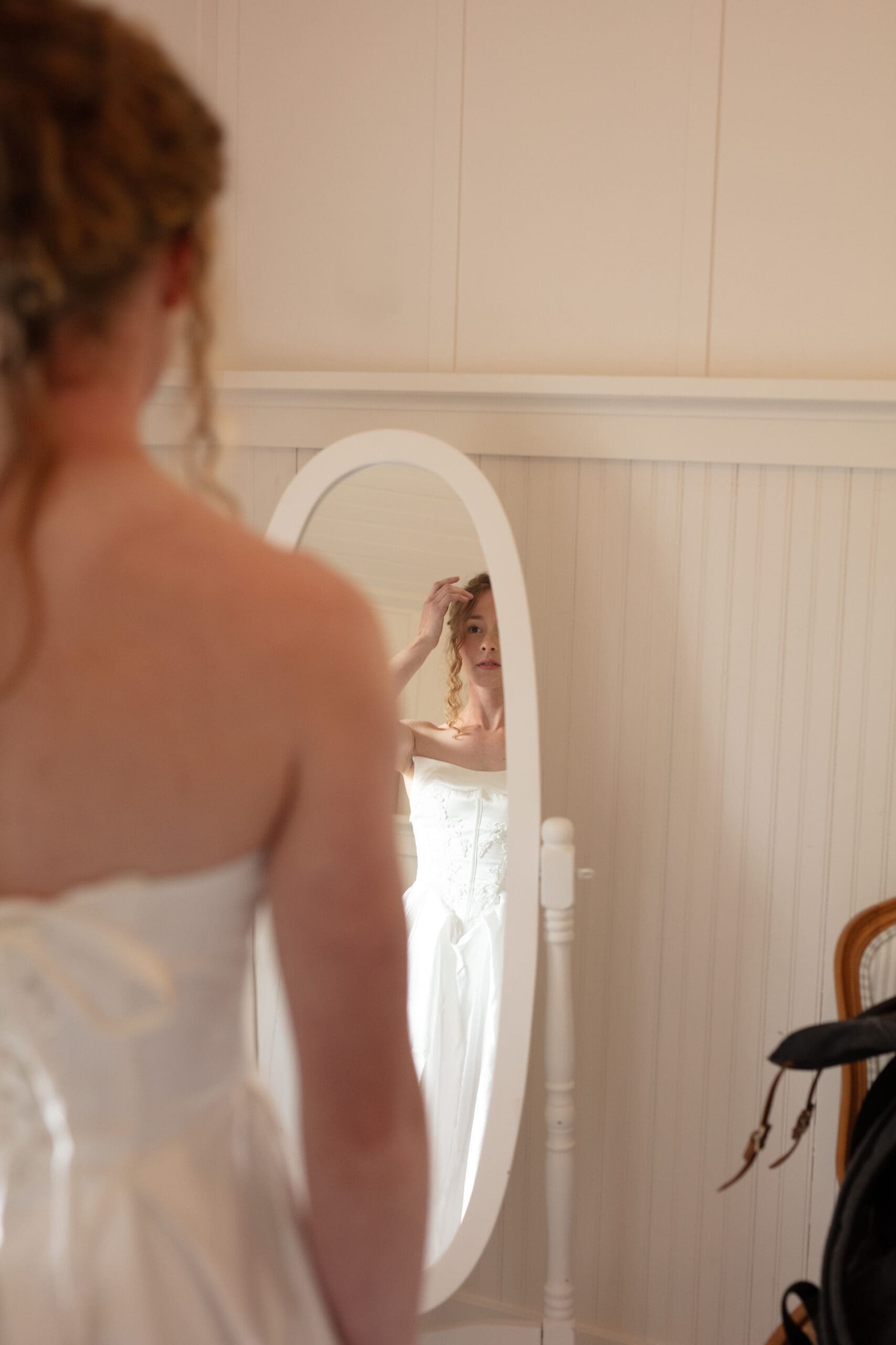 A reflective moment as the bride adjusts her hair in the mirror before her Christianson's Nursery wedding.