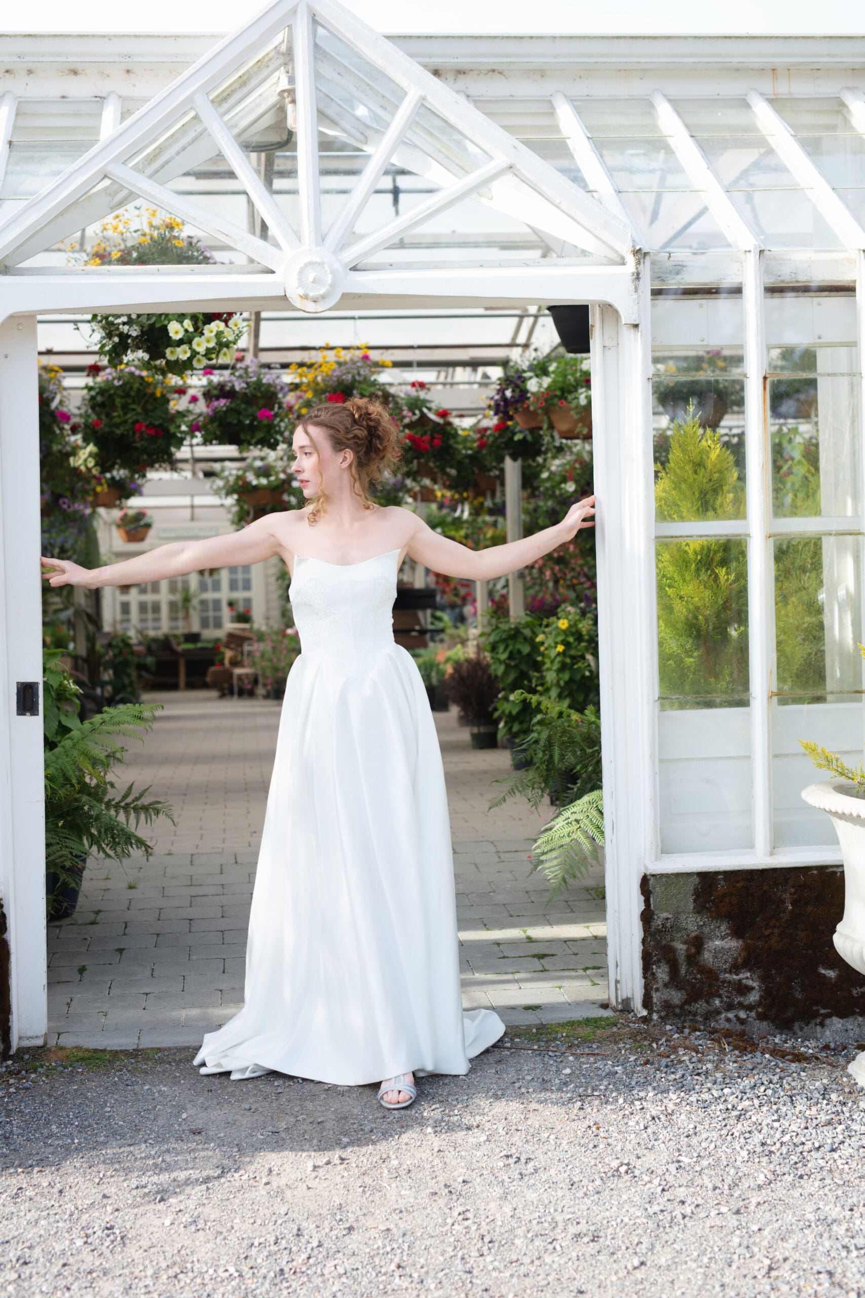Bride stands in the greenhouse doorway at Christianson's Nursery, framed by hanging baskets and historic charm