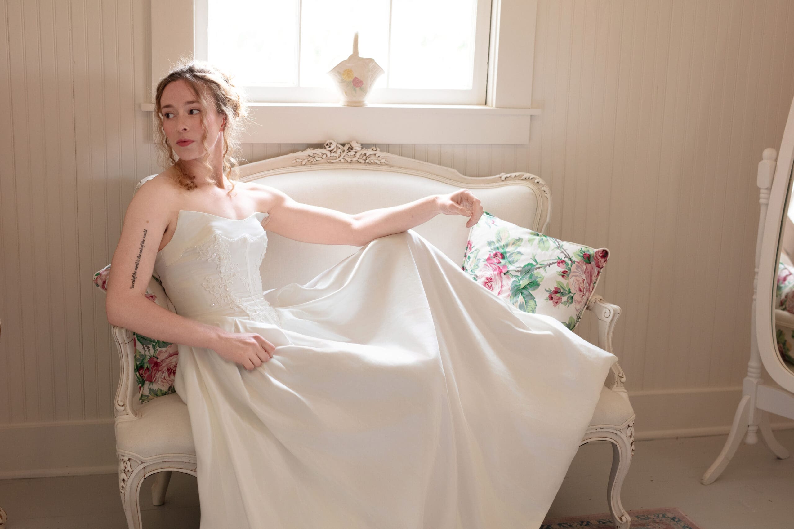 Bride in a vintage-inspired gown sits by the window in a quiet bridal suite at Christianson's Nursery.