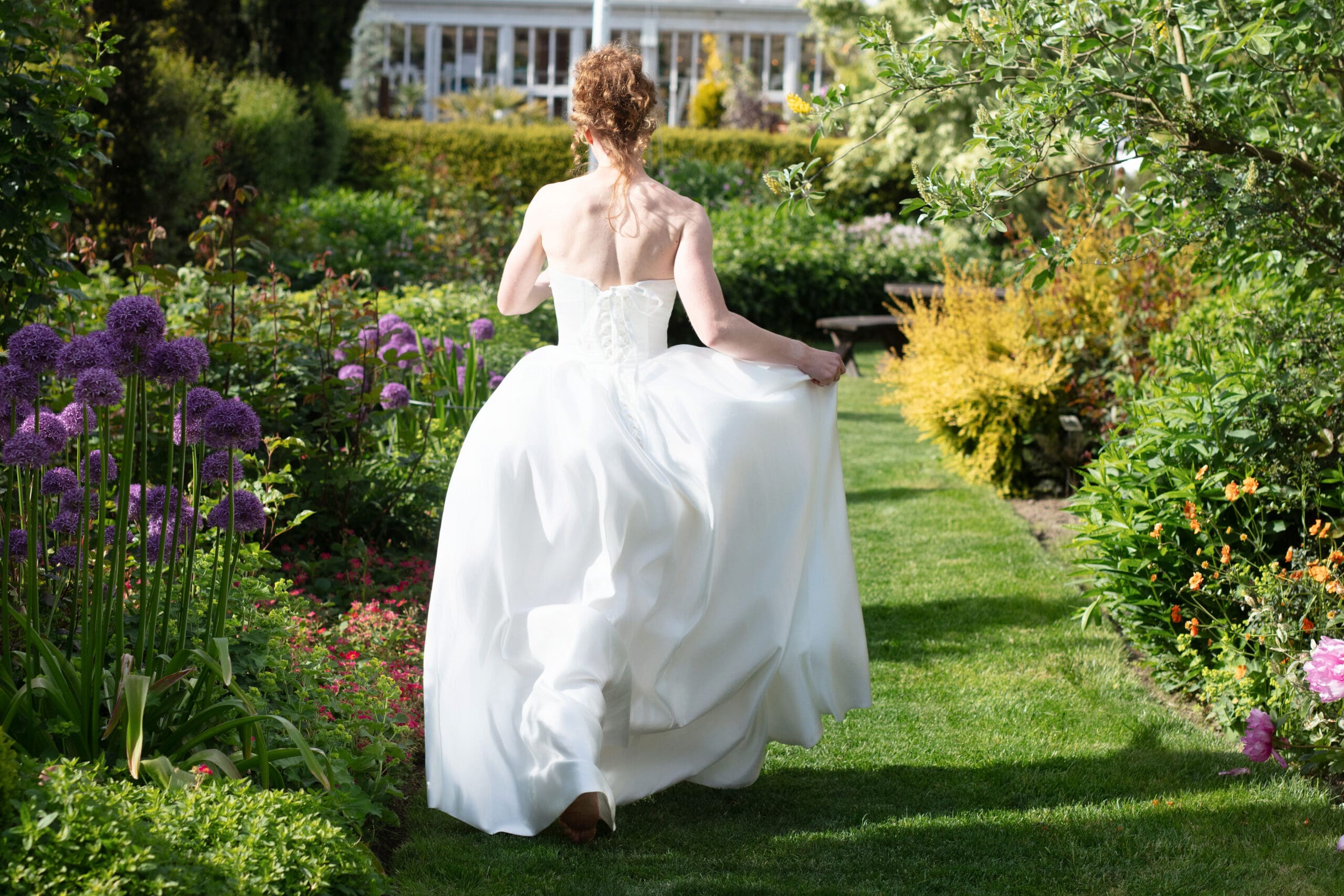 Bride walks through the lush garden path, dress flowing behind her at Christianson's Nursery.