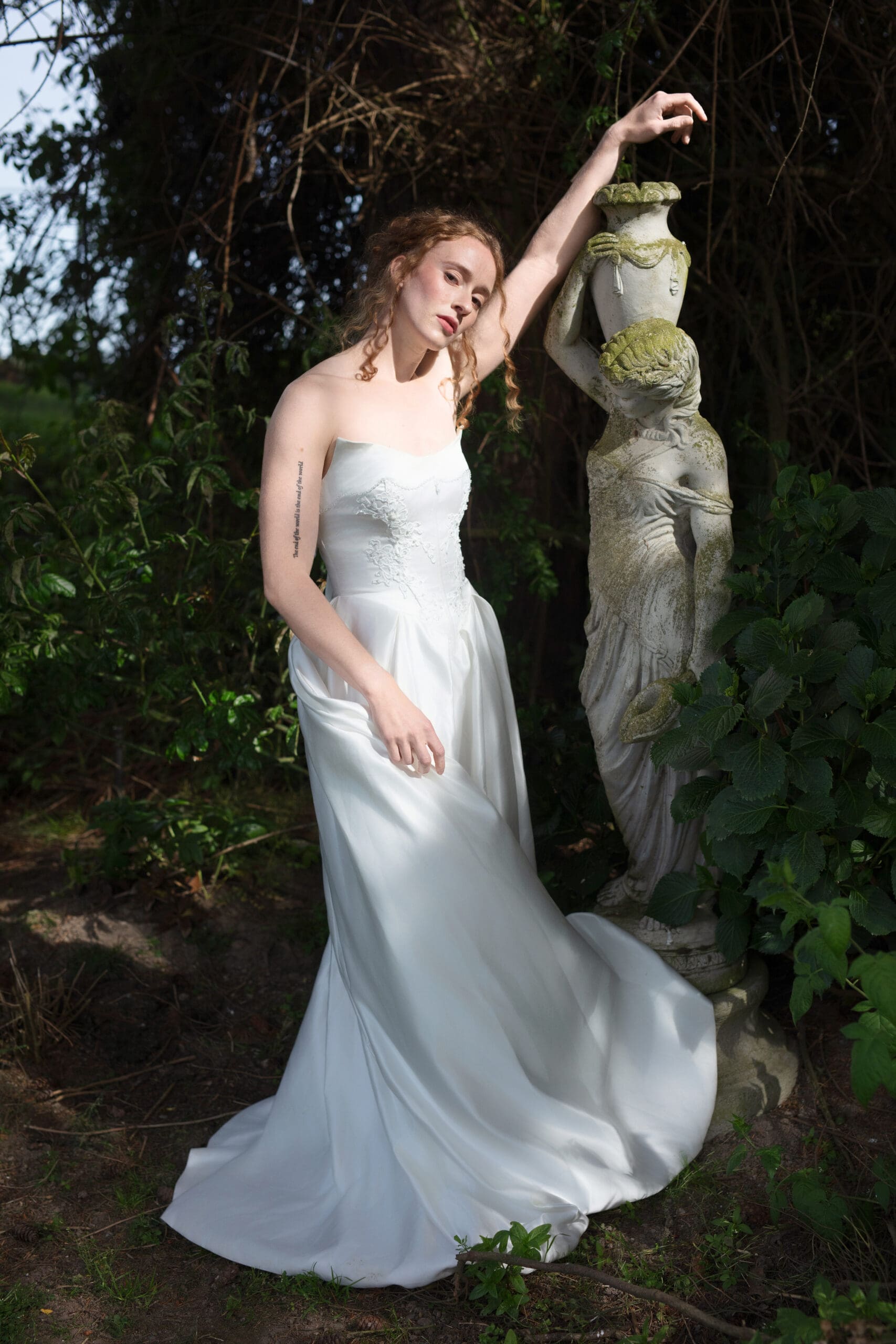 Moody portrait of the bride standing beside a weathered statue, evoking a timeless, romantic Christianson’s Nursery wedding aesthetic.