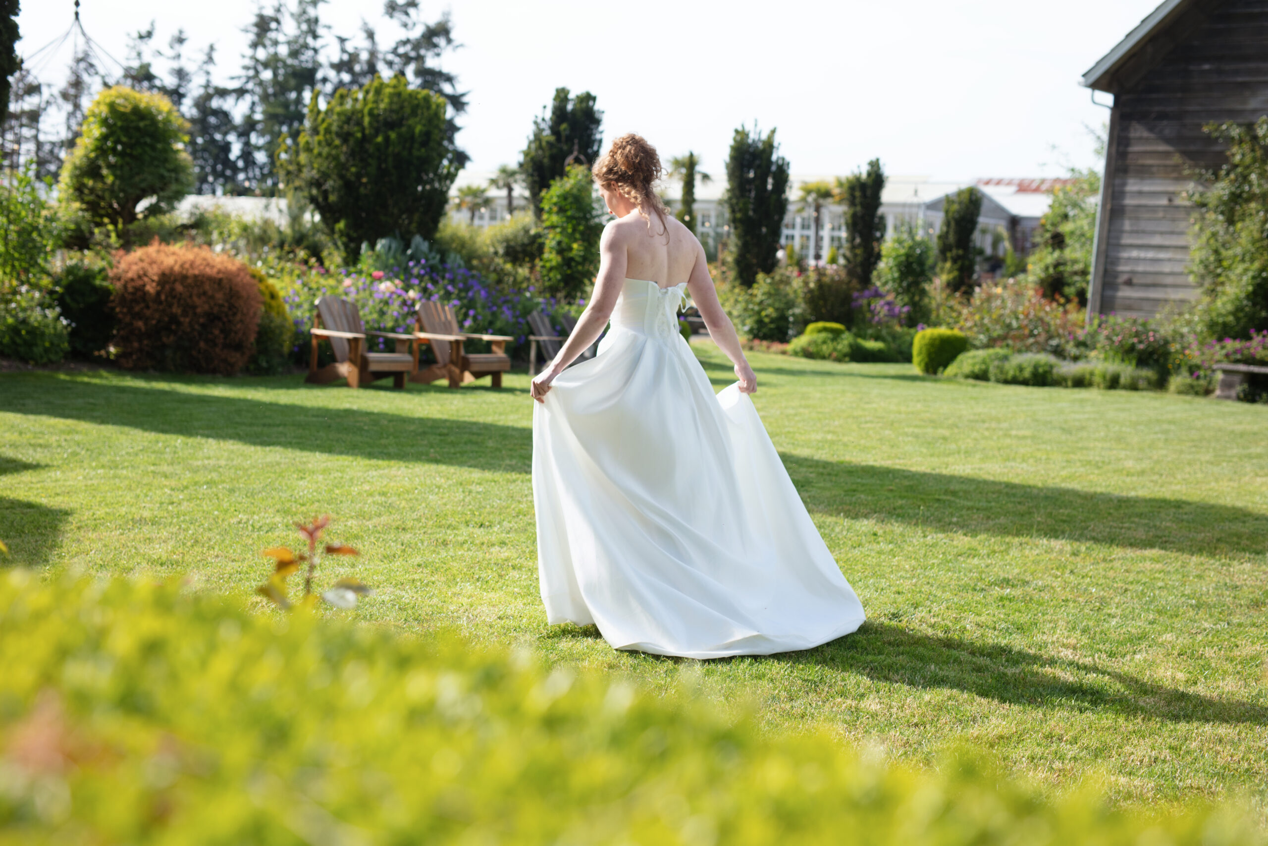 Back view of bride walking through the lawn at Christianson’s Nursery wedding, gown trailing behind her in golden light.