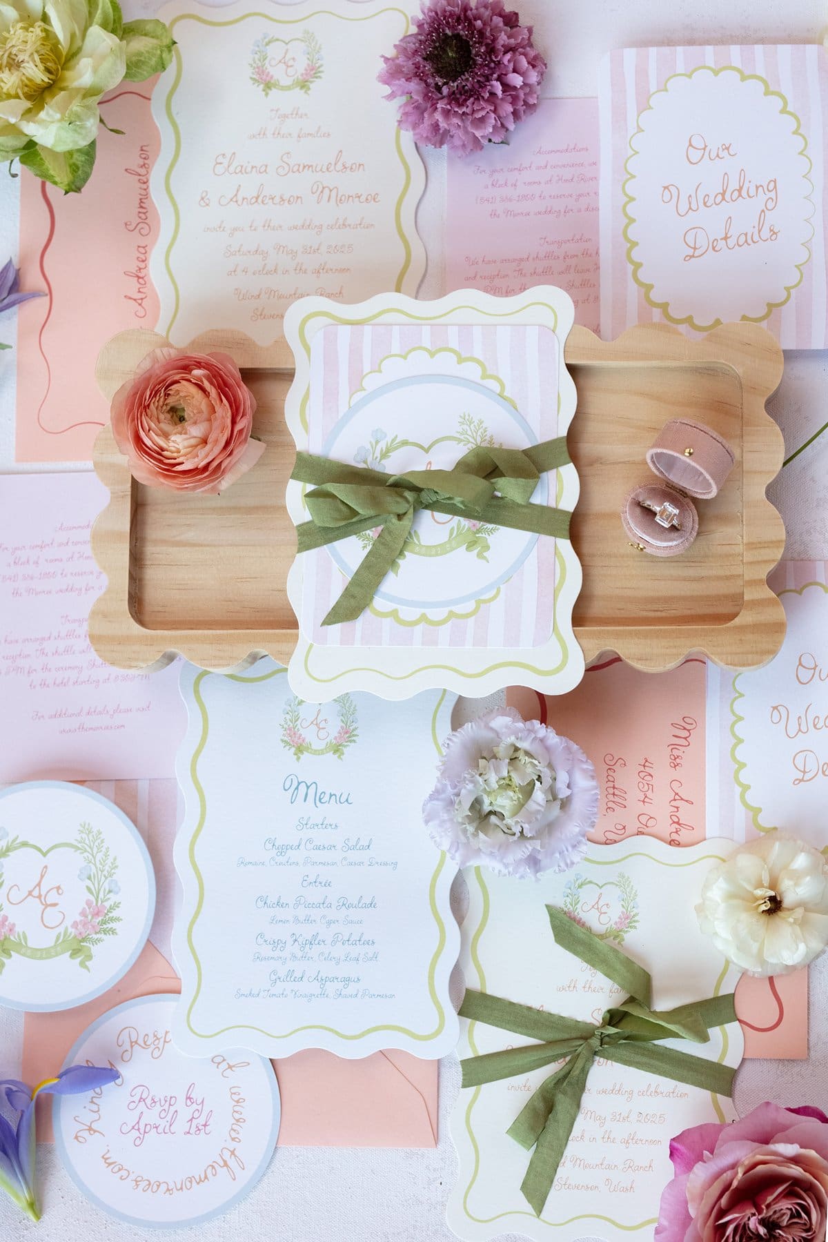 Pastel wedding invitation suite flat lay with custom stationery, velvet ring boxes, and fresh blooms.