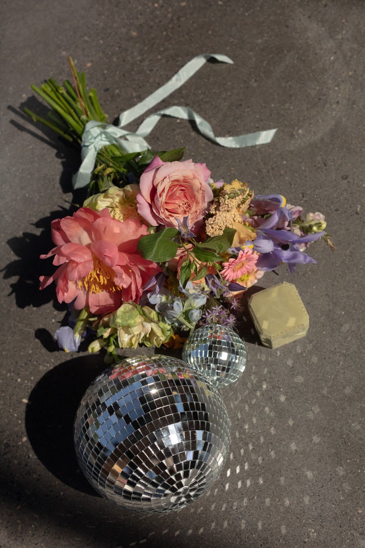 Bold bridal bouquet with pink and peach florals styled next to disco balls for a modern wedding flat lay.