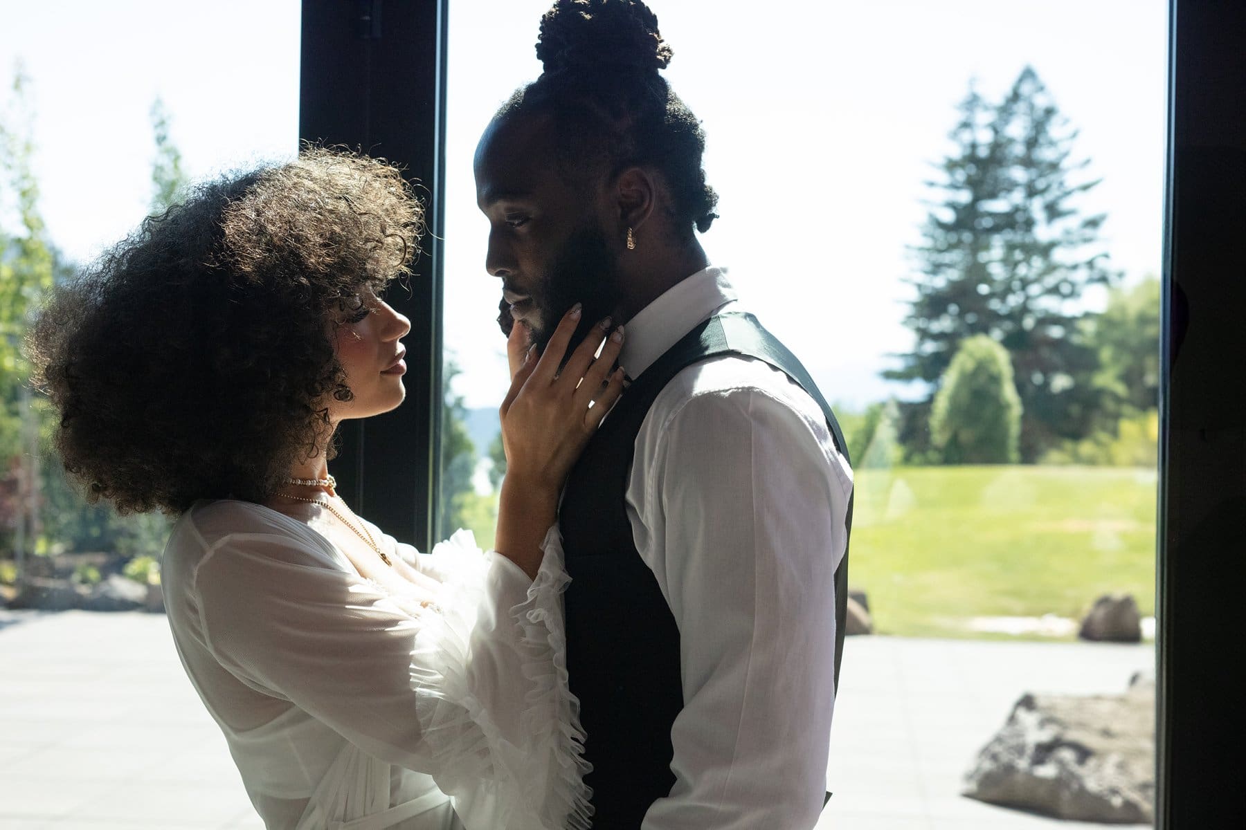 Newlyweds share a tender look indoors with backlit natural light pouring in through glass windows.