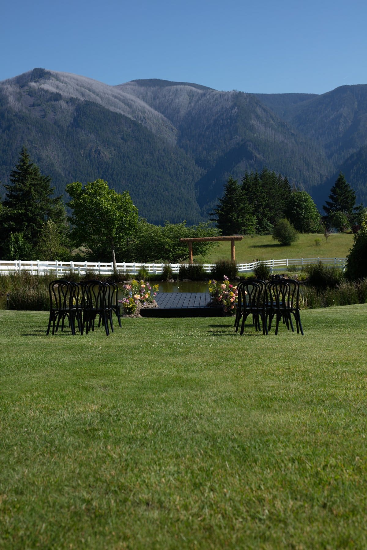 Black chairs arranged for outdoor ceremony by the dock and pond with mountain views.