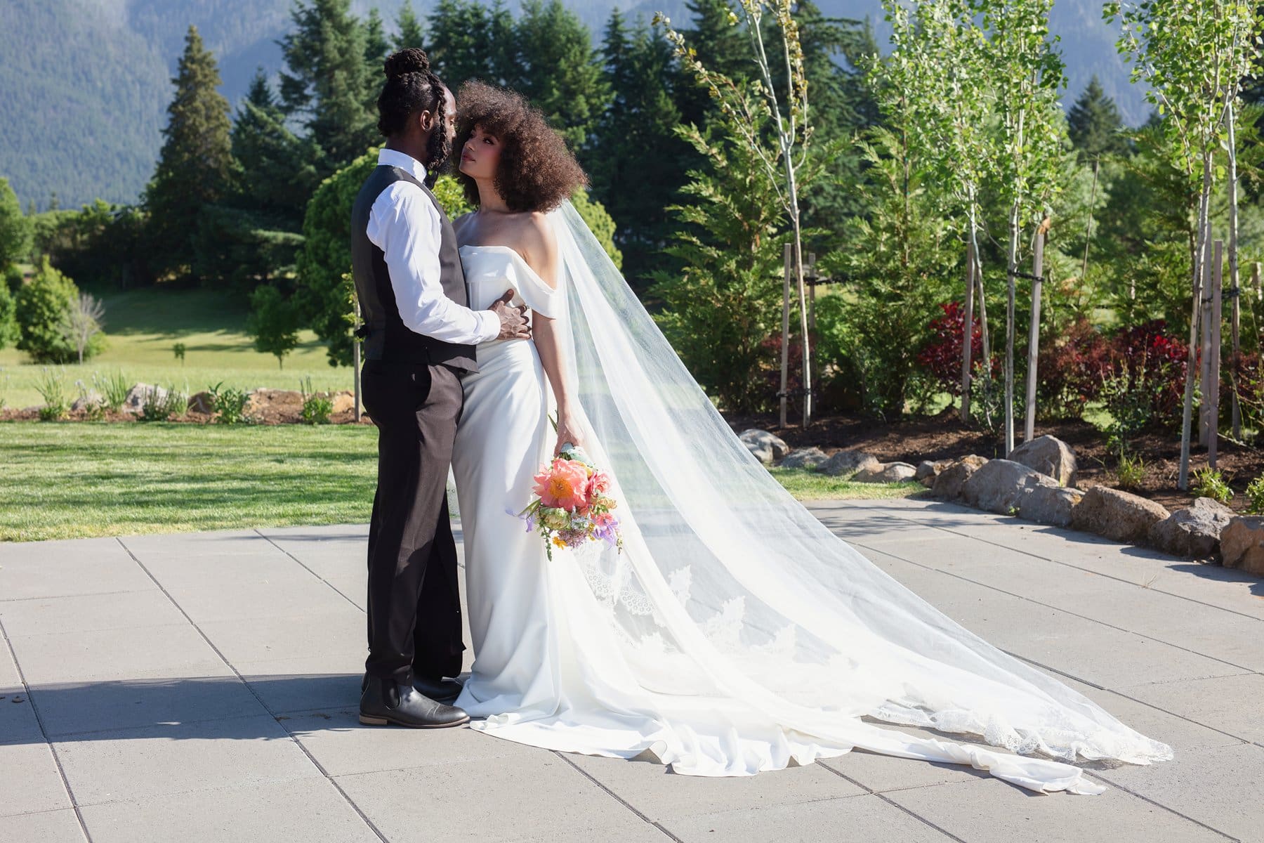 Bride and groom standing forehead to forehead with a long flowing veil and bright bouquet outside their Wind Mountain Ranch venue