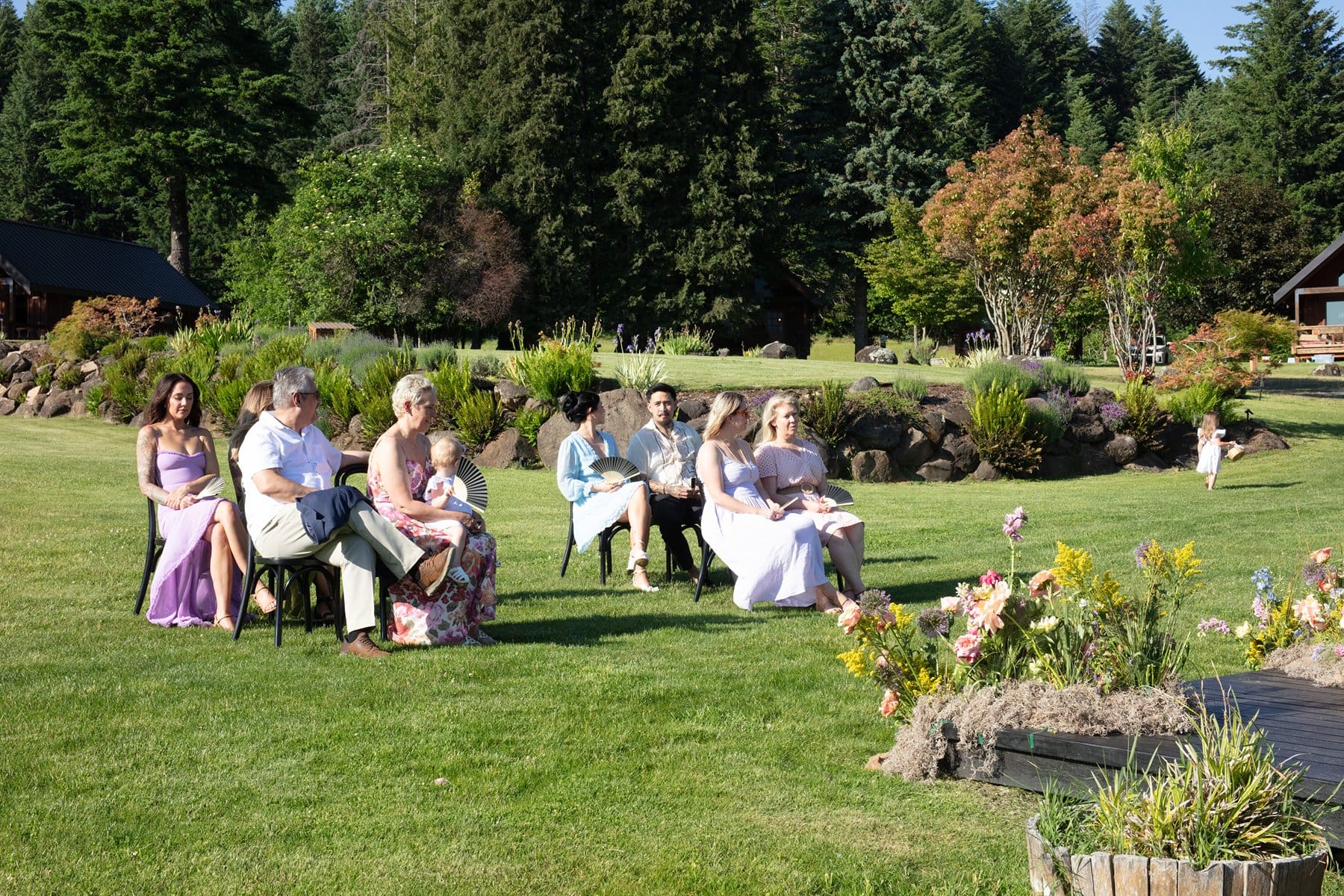 Guests seated on the lawn during an outdoor ceremony at Wind Mountain Ranch venue, surrounded by wildflowers and forested views.