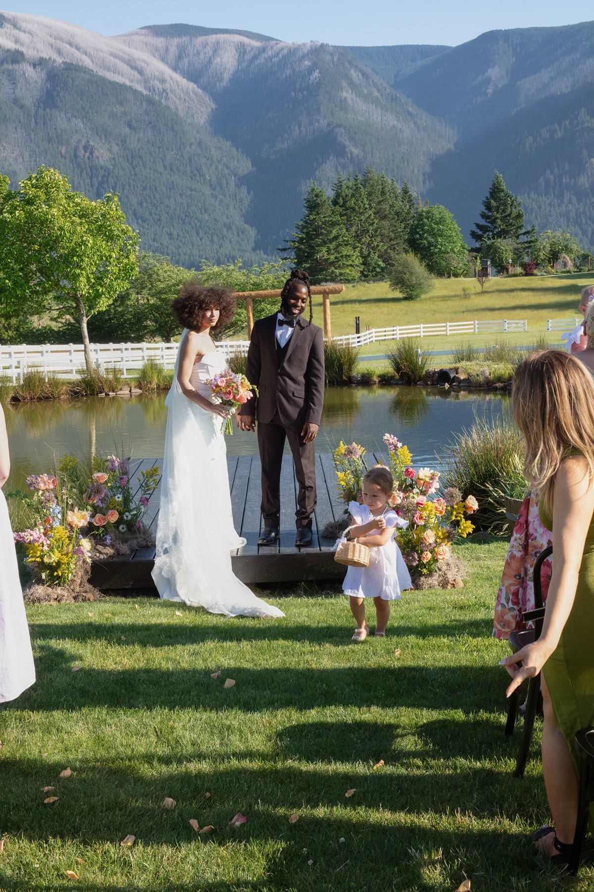 he bride and groom stand on the dock as their flower girl tosses petals during the ceremony.