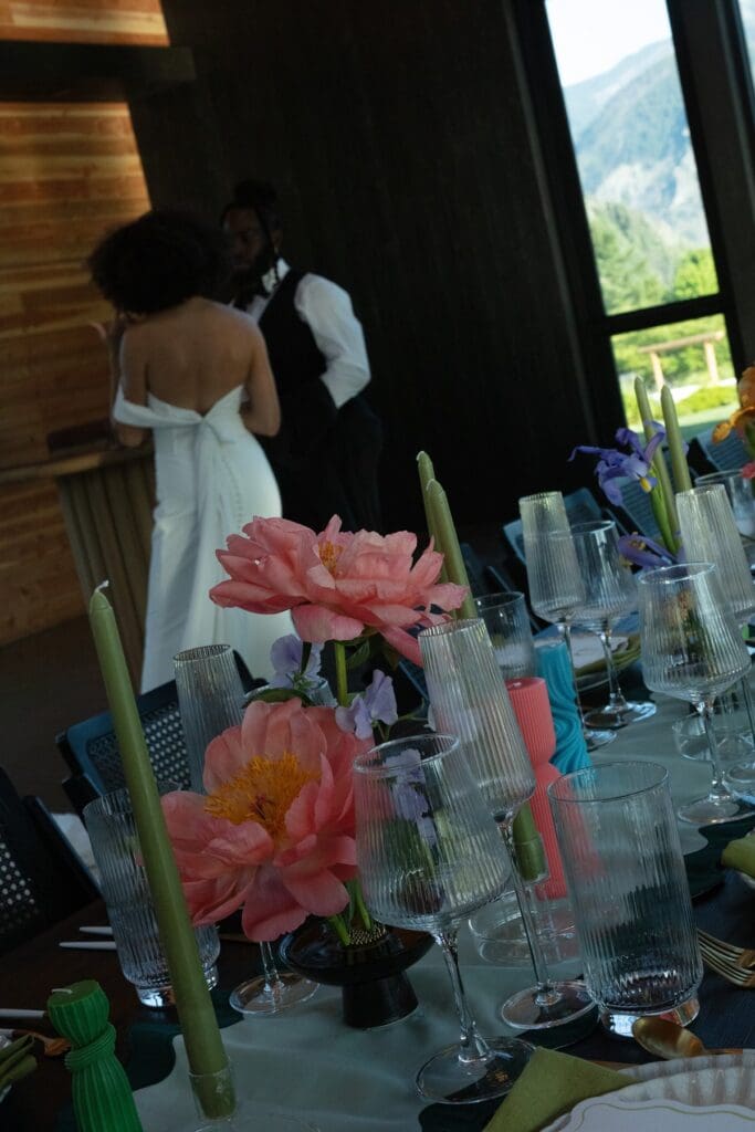 Colorful floral centerpiece and taper candles in the foreground, while the bride and groom dance softly behind at Wind Mountain Ranch venue.