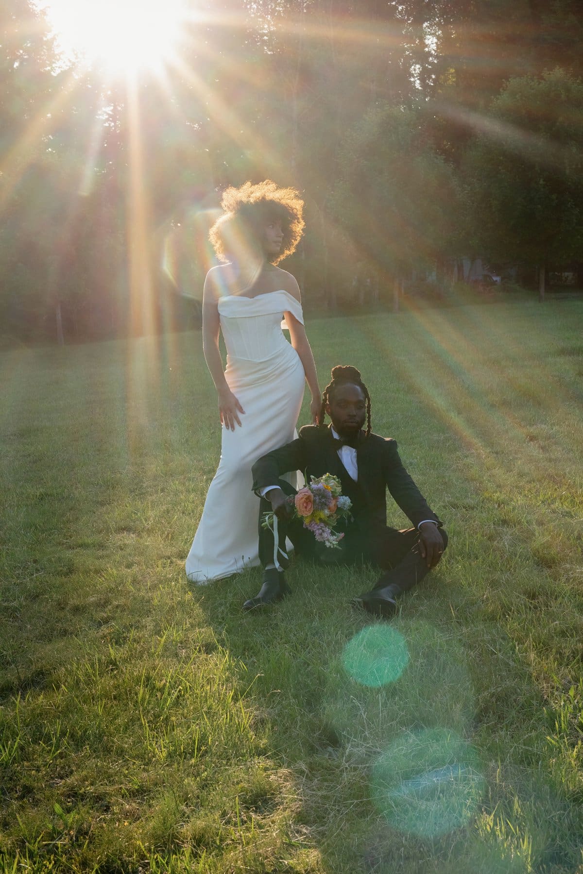 The couple poses in a sun-drenched field with radiant flares shining behind them at Wind Mountain Ranch venue.