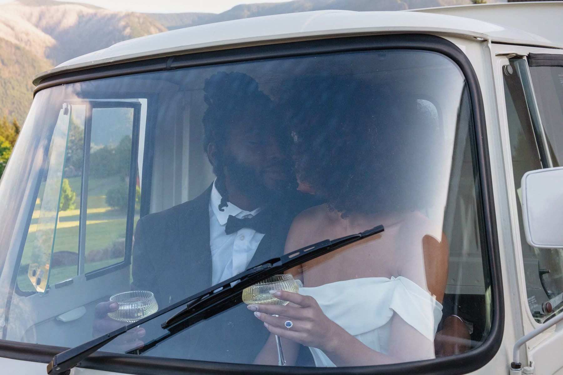 Newlyweds share a quiet toast inside a vintage van, champagne glasses in hand and smiles through the windshield.