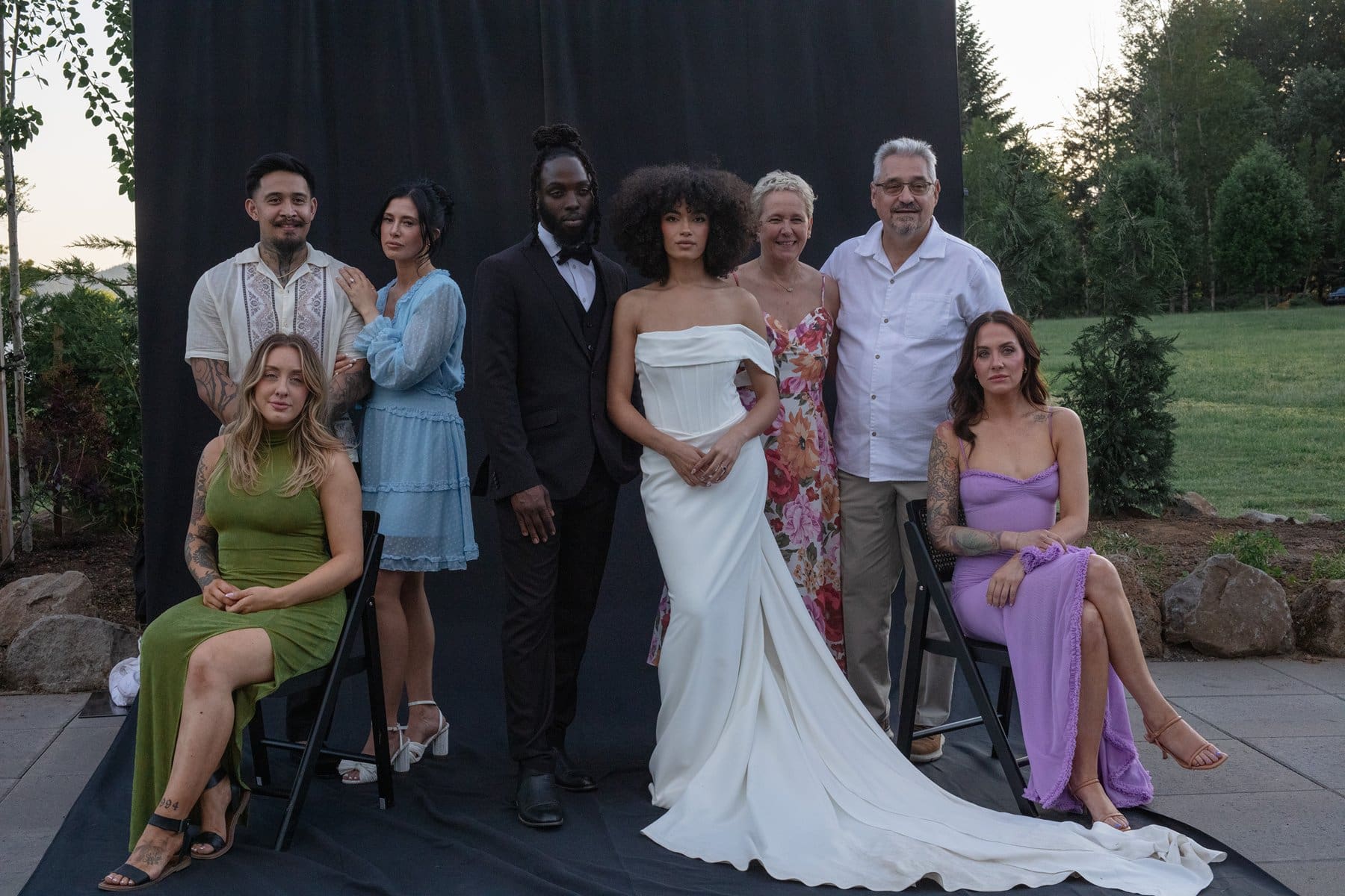 Bride and groom pose with close family members in front of a black backdrop, blending elegance with candid warmth.