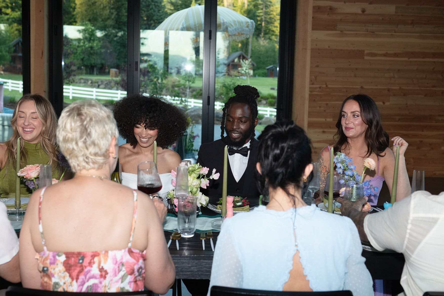 Bride and groom sit together smiling at the head of the dinner table, surrounded by guests at Wind Mountain Ranch.