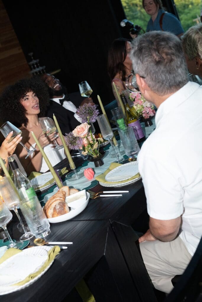 Bride and groom share a laugh with guests during the wedding dinner, surrounded by florals, wine, and candlelight.