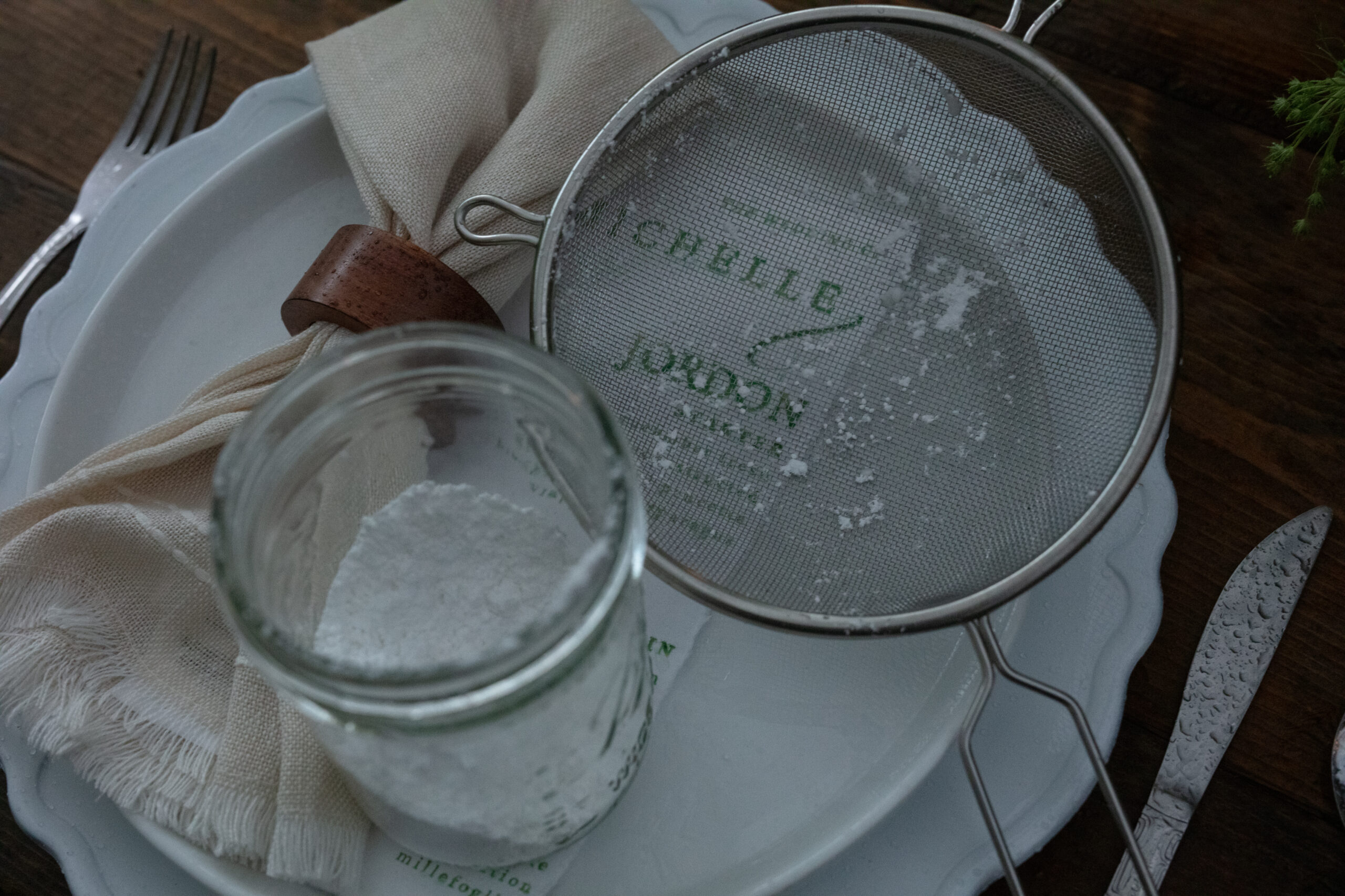 Table setting with personalized plate featuring couple’s names, vintage sieve, and powdered sugar – charming and rustic ideas for weddings.
