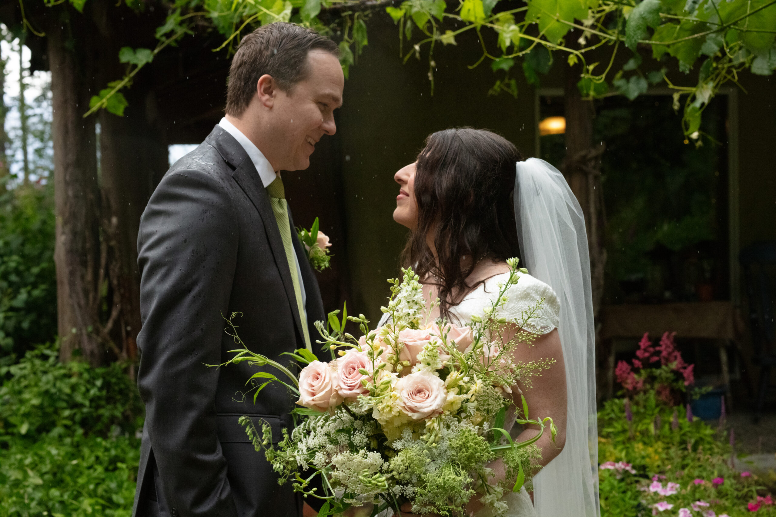 Bride and groom smile at each other surrounded by greenery and soft rain, showing how natural backdrops can inspire unique ideas for weddings in Washington.