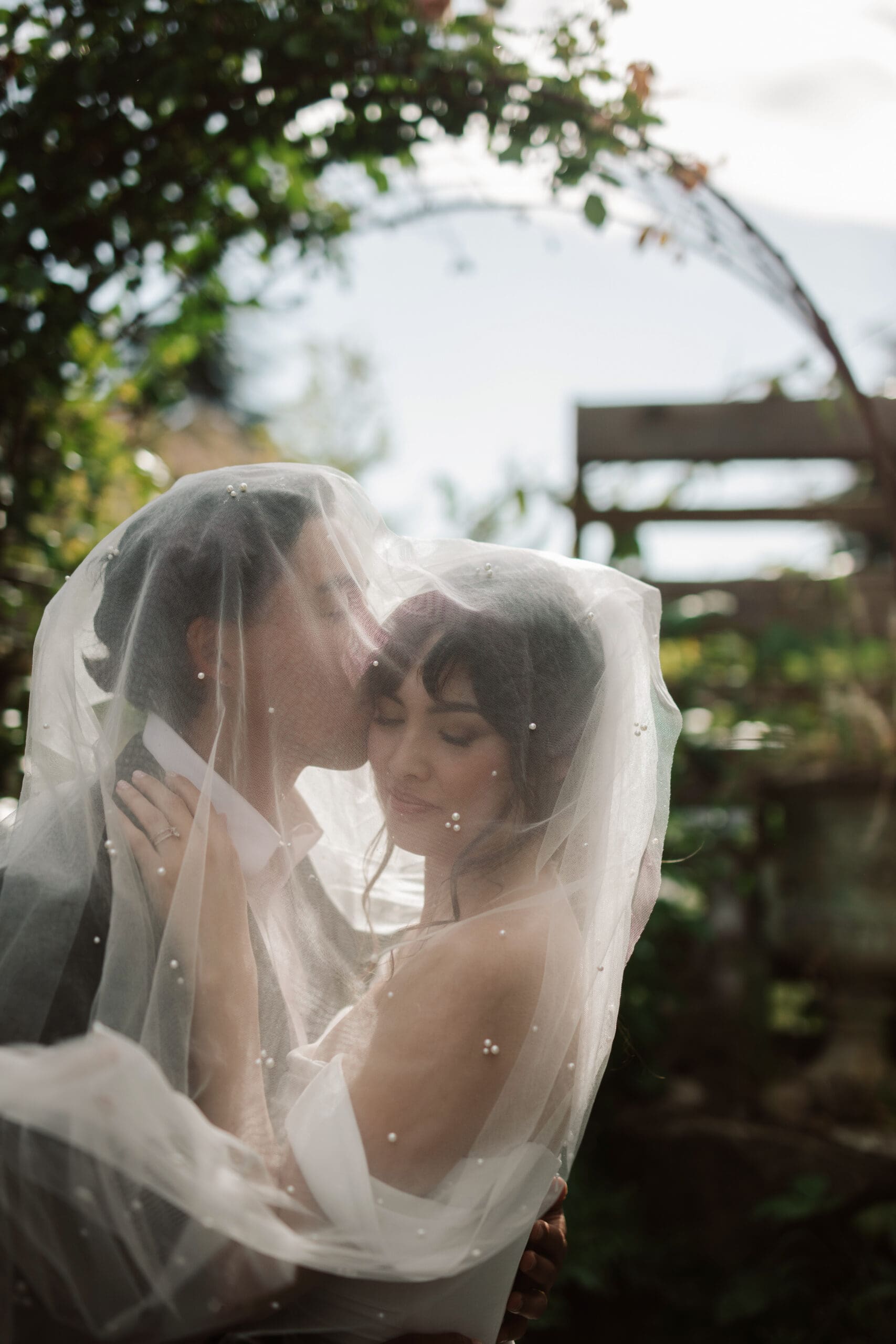 Romantic veil shot of newlyweds, capturing quiet connection—an emotional and artistic wedding moment.