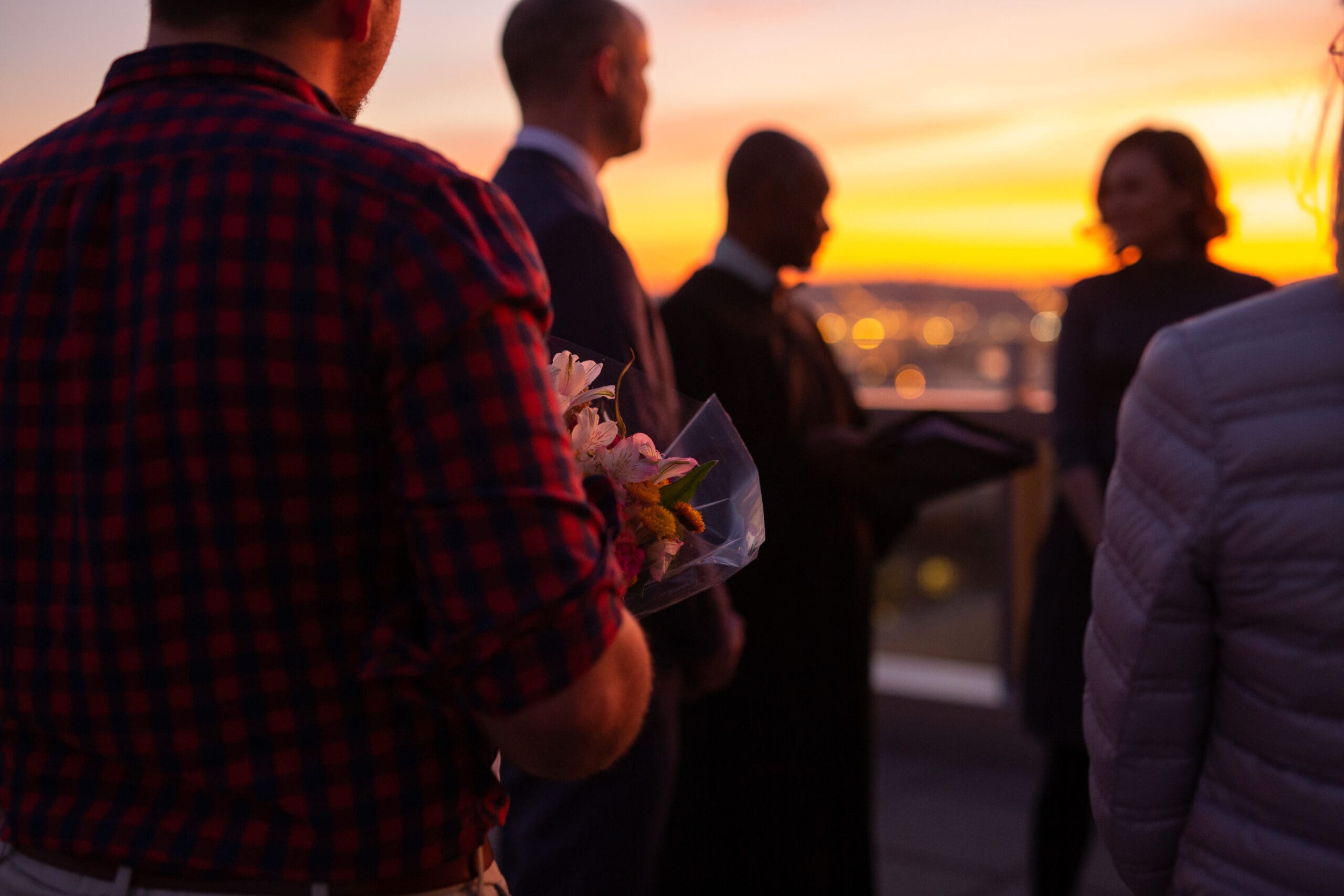 Rooftop ceremony at sunset with guests and officiant silhouetted in golden light – stunning urban elopement ideas for weddings.