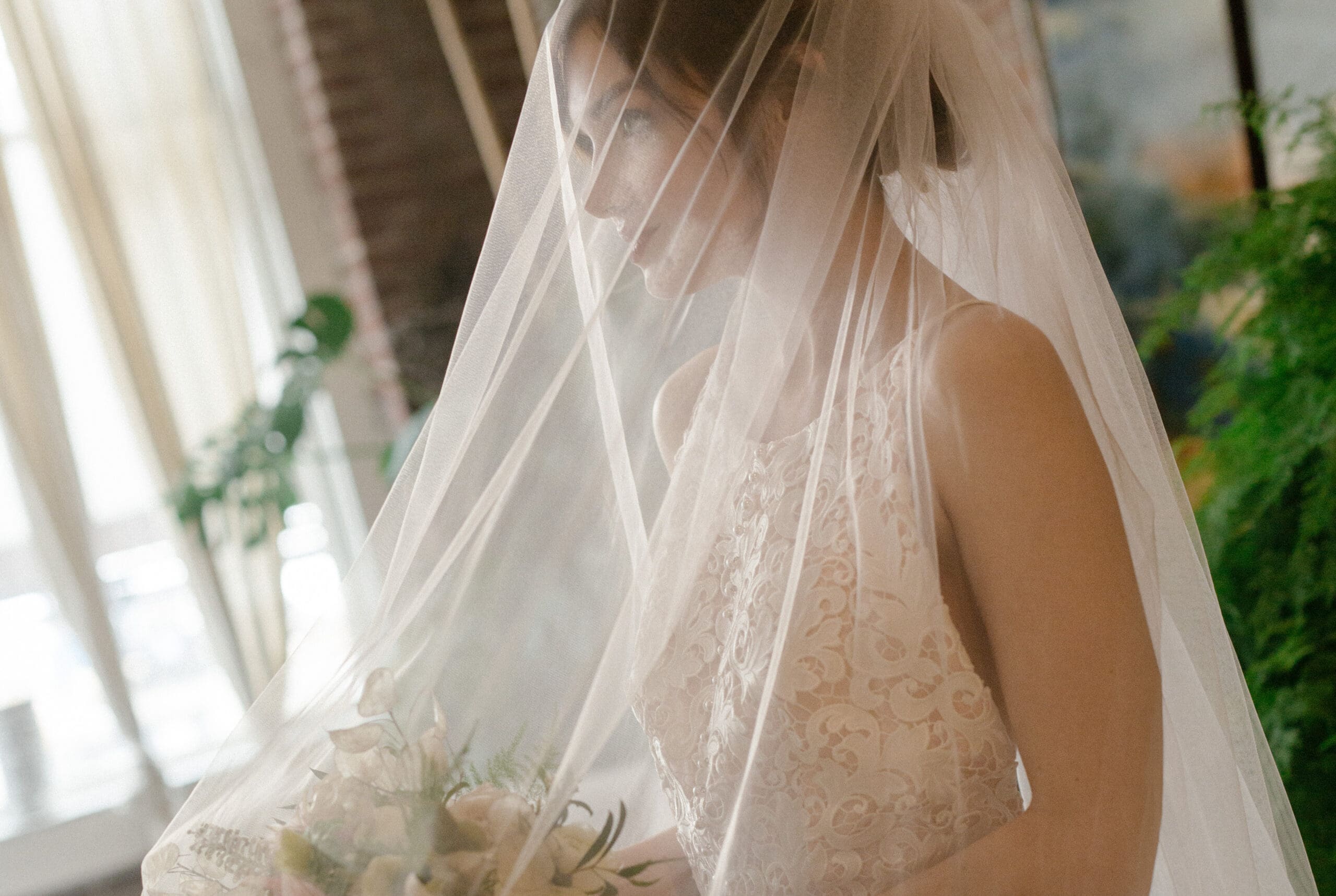Close-up of bride standing under a sheer veil with soft lighting, a quiet moment that reflects personal ideas for weddings centered around emotion and style.