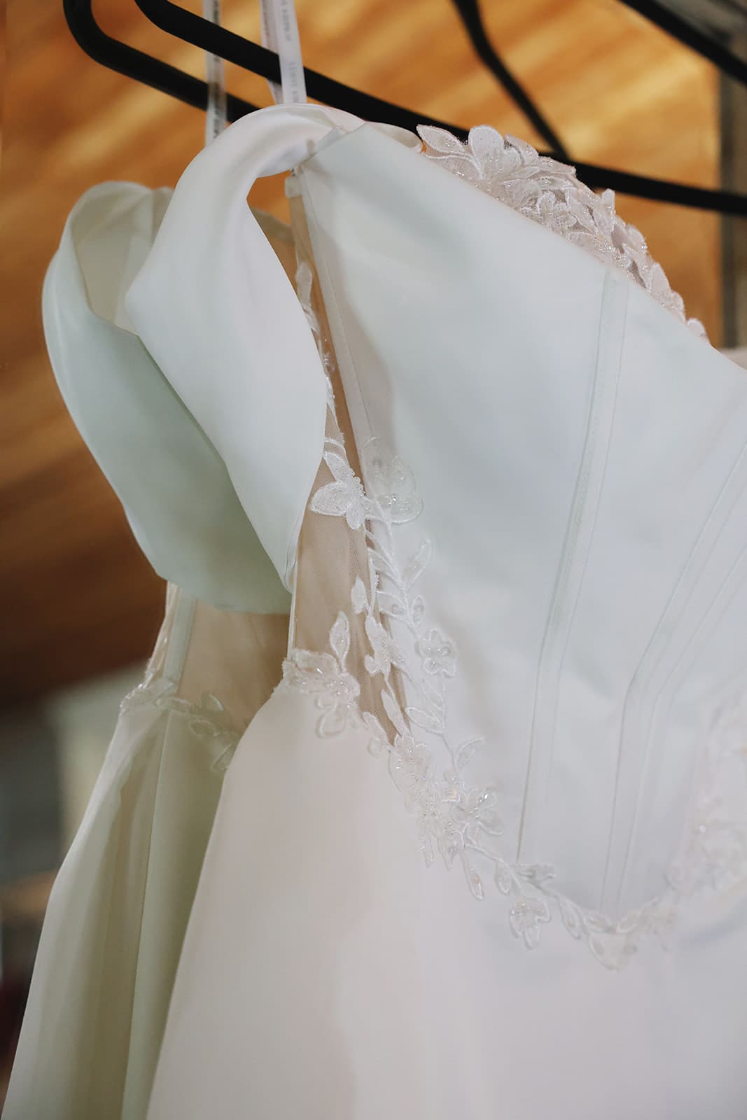 Wedding dress hanging in soft natural light, showcasing the delicate lace and off-the-shoulder structure before the ceremony begins.