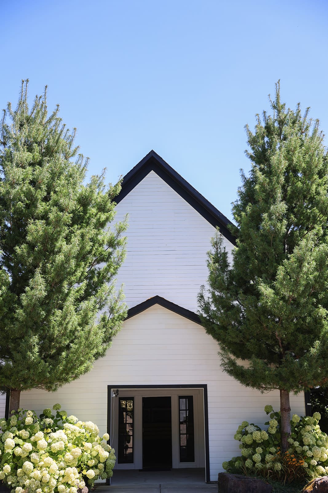 Reception building at Cape Horn Estate, a charming white barn surrounded by summer greenery in Oregon.