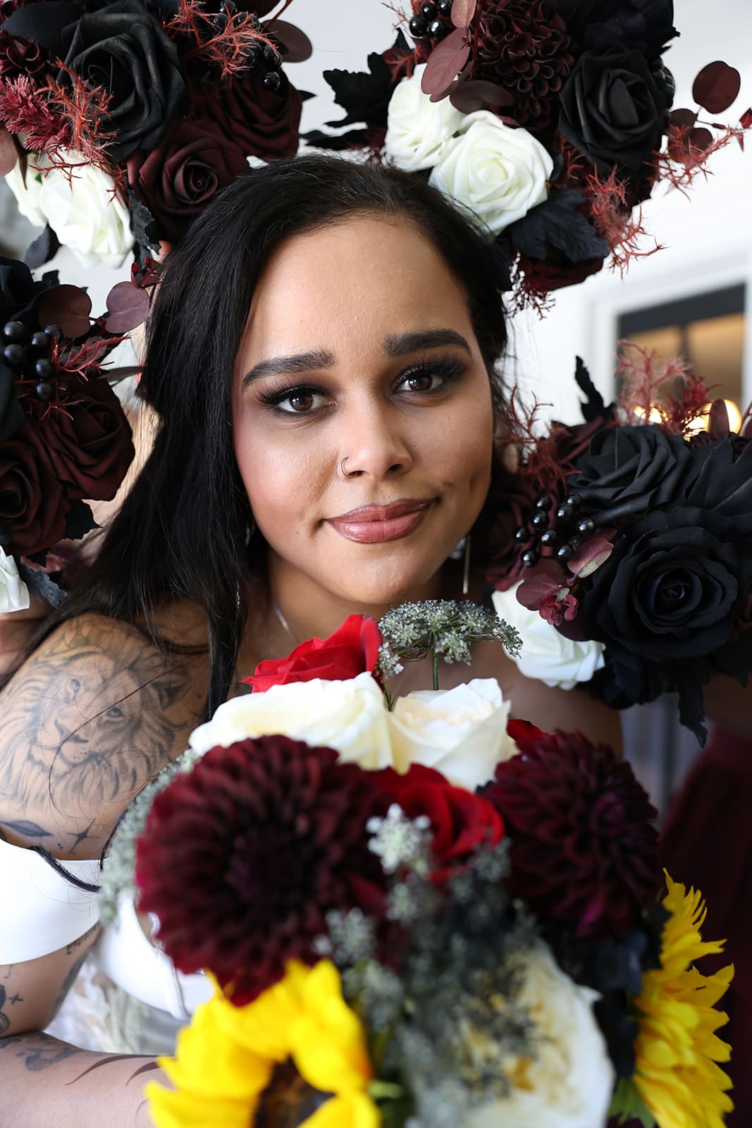 Bride holds a vibrant bouquet of sunflowers, dahlias, and roses, framed by dark and ivory silk floral headpieces.