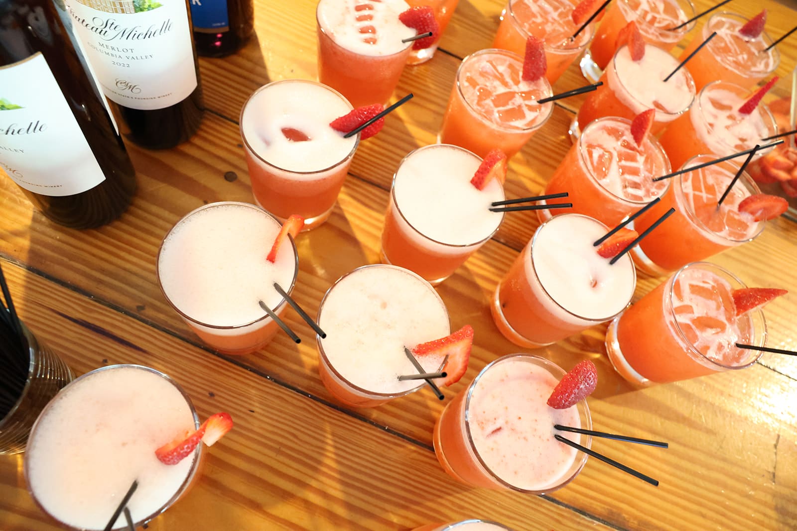 Glasses of vibrant strawberry cocktails with frothy tops and fresh fruit garnishes sit ready for guests on a wood table during cocktail hour at this Oregon wedding venue.