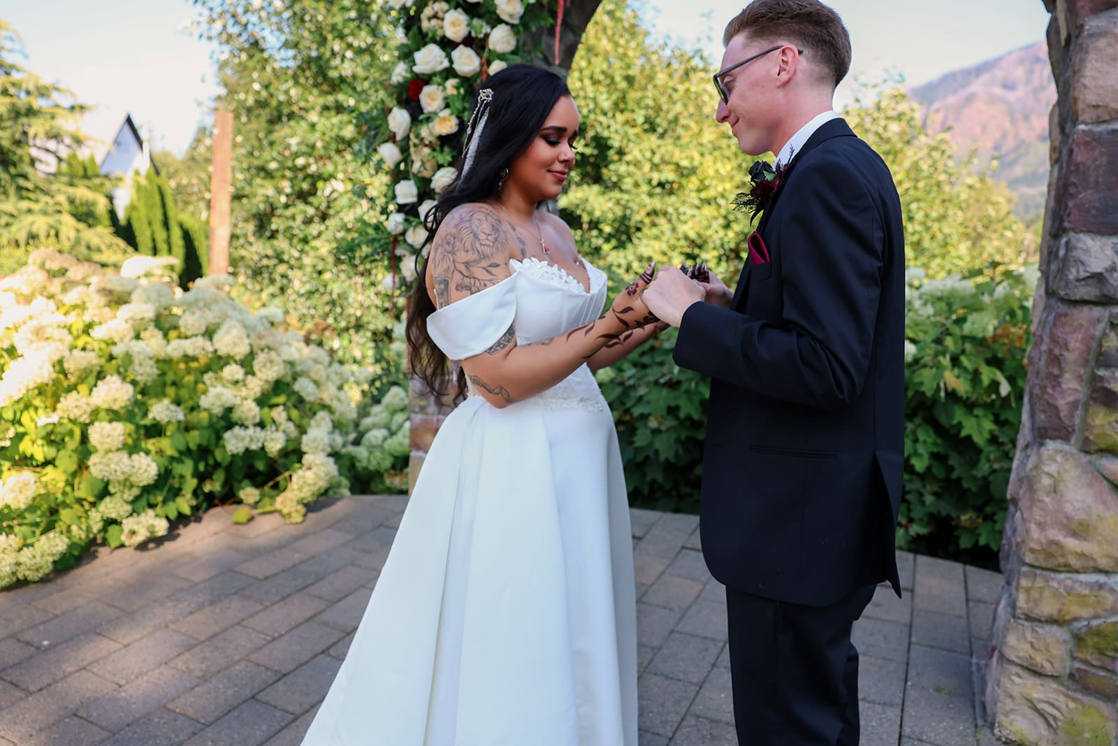 Groom places a ring on the bride’s hand during their ceremony at an intimate Oregon wedding venue with a romantic floral arch.