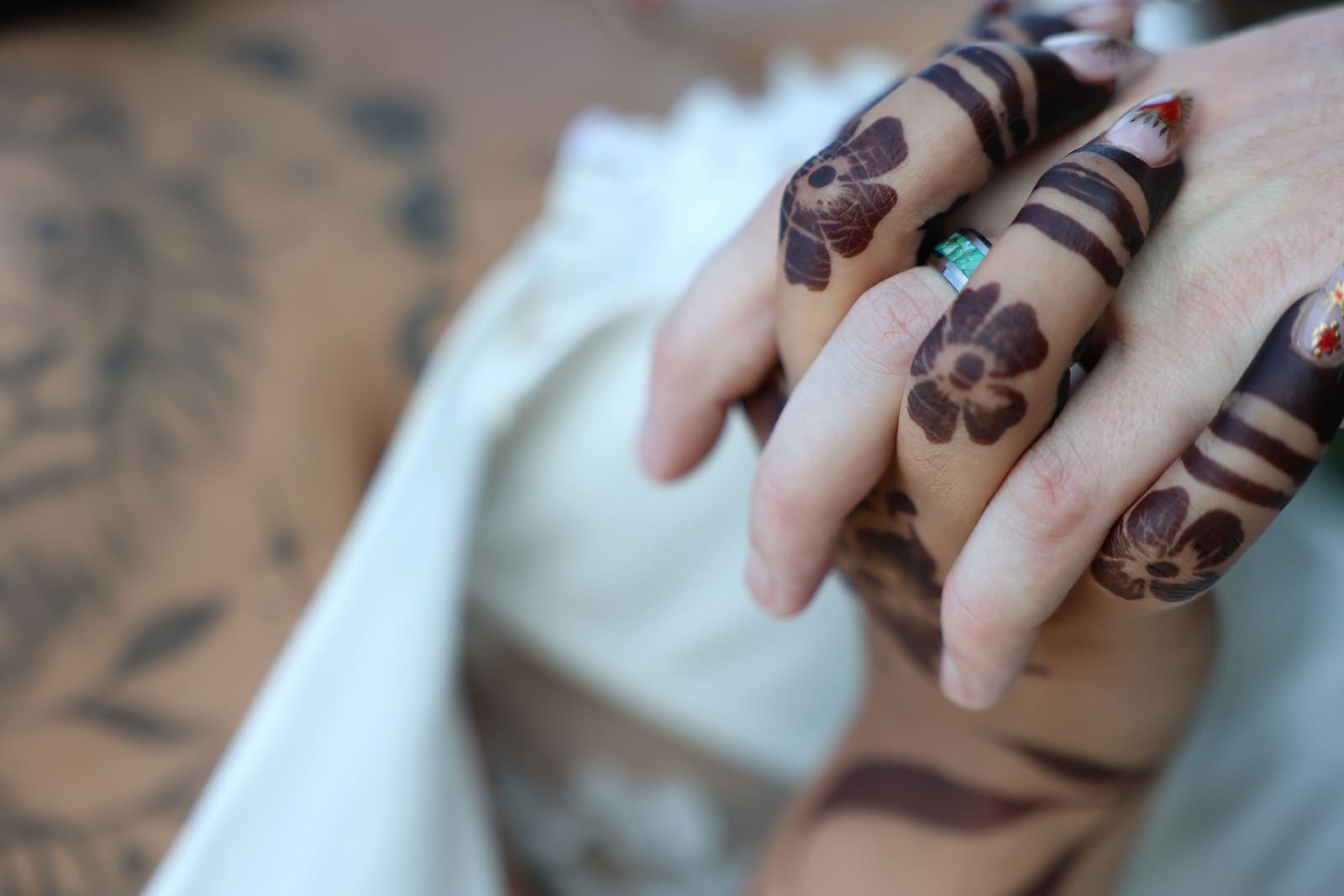 A detailed shot of the couple’s hands intertwined, showcasing the bride’s floral henna design and sparkling engagement ring resting on the folds of her dress.