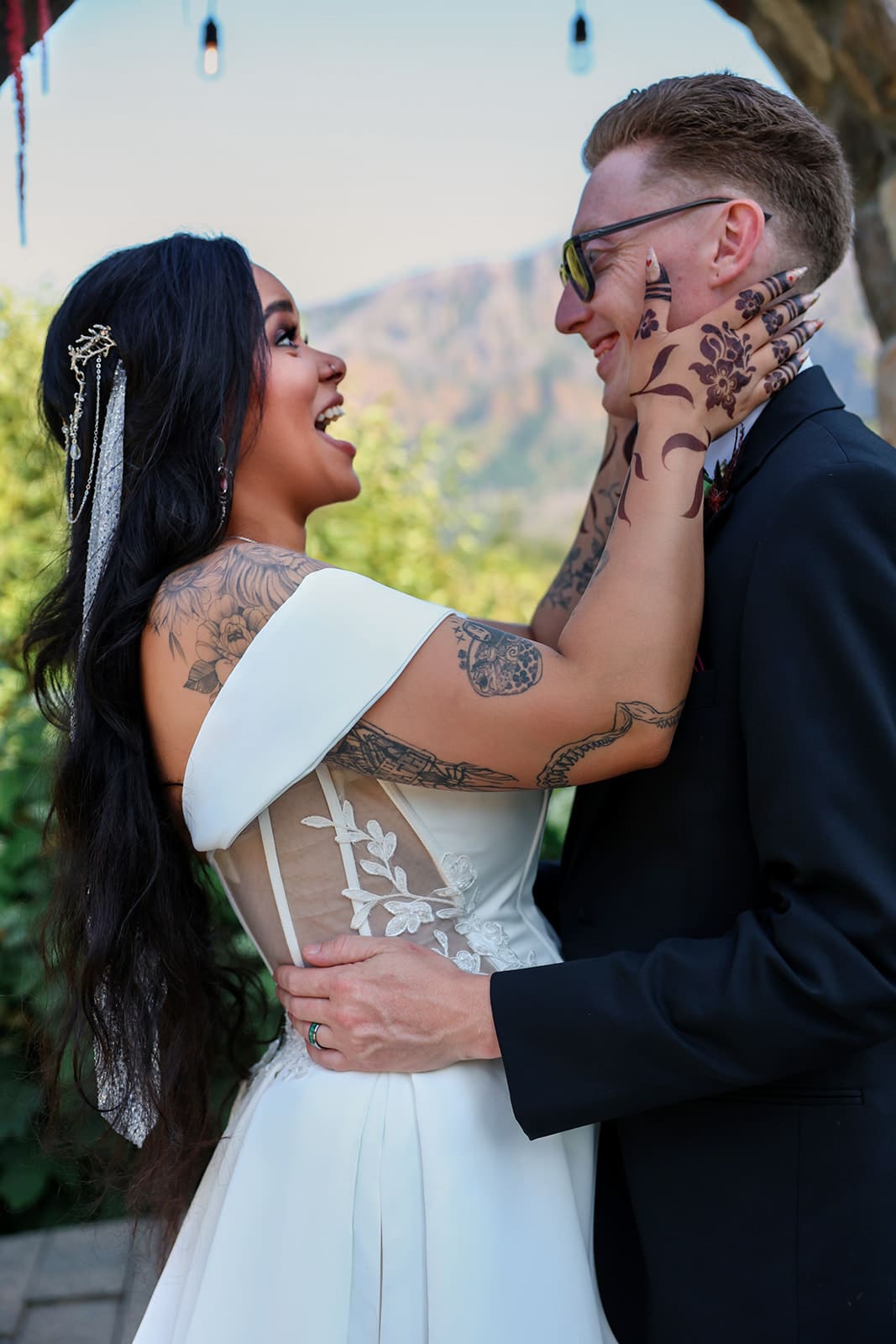 Candid moment between bride and groom under string lights, captured with forested Oregon mountains in the background.