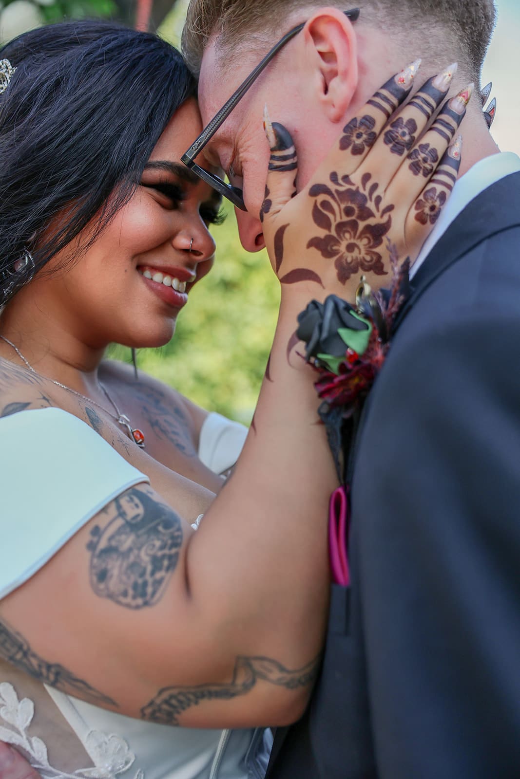 Close-up of the bride smiling with her hands on the groom’s face, their foreheads touching as she shows off intricate henna and tattoos.
