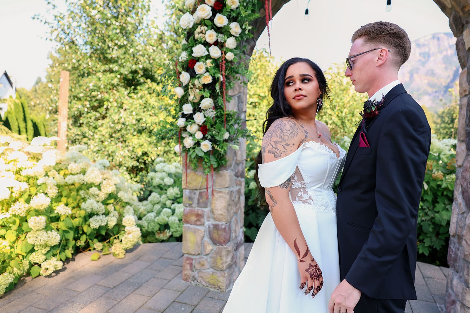 Bride and groom stand hand-in-hand beneath a flower-covered arch, sharing a quiet moment together.