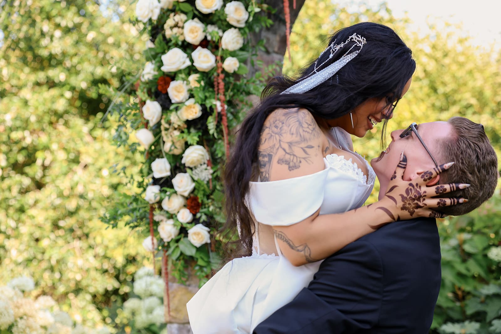 Close-up of groom lifting bride in front of a lush floral arch, both smiling with joy during their ceremony at an Oregon wedding venue.